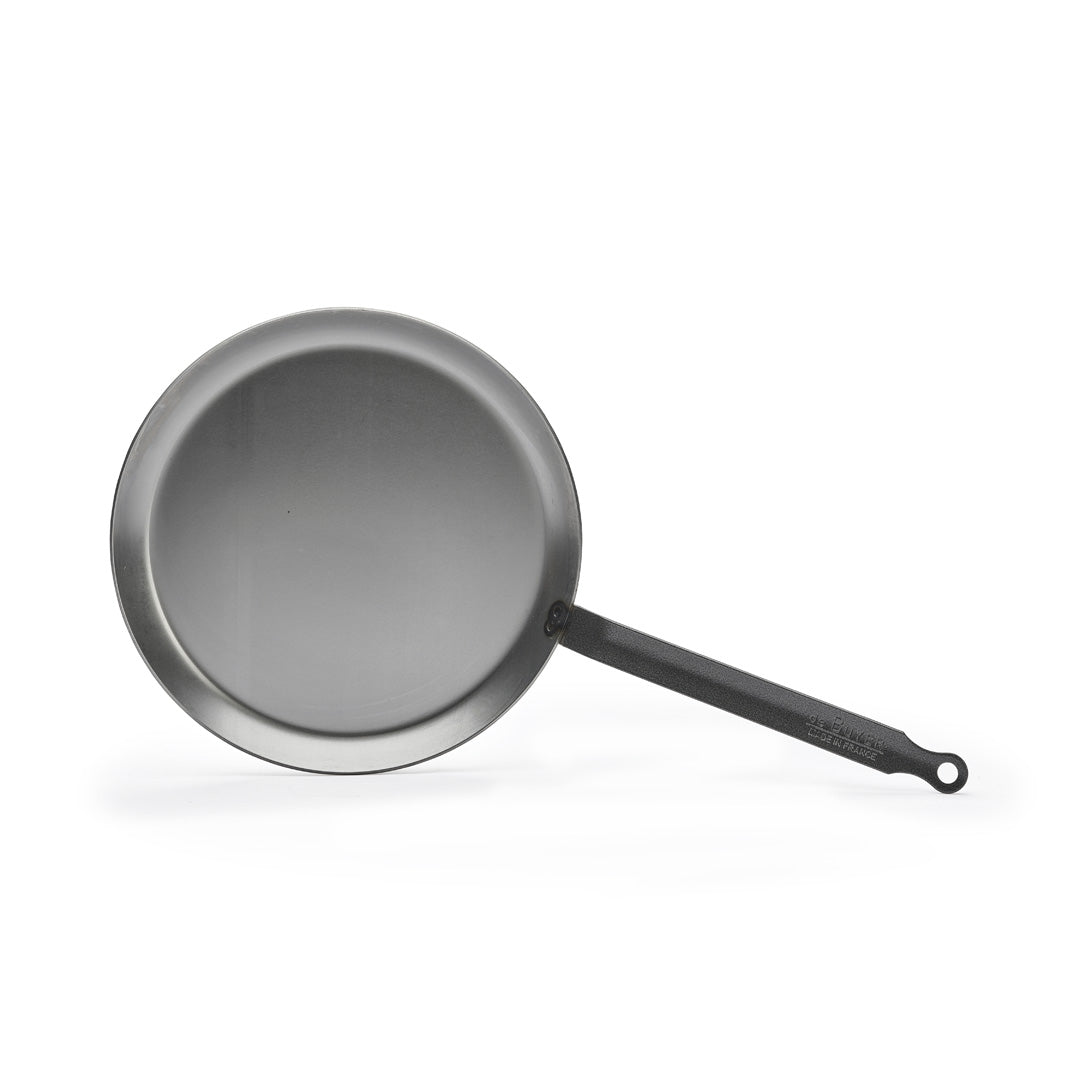 Eine De Buyer Crêpe-Pfanne Carbone Plus mit langem schwarzem Griff steht auf weißem Grund. Die runde, flache Metallpfanne hat eine glatte, ebene Oberfläche und ist damit ideal für perfekte Crêpes.
