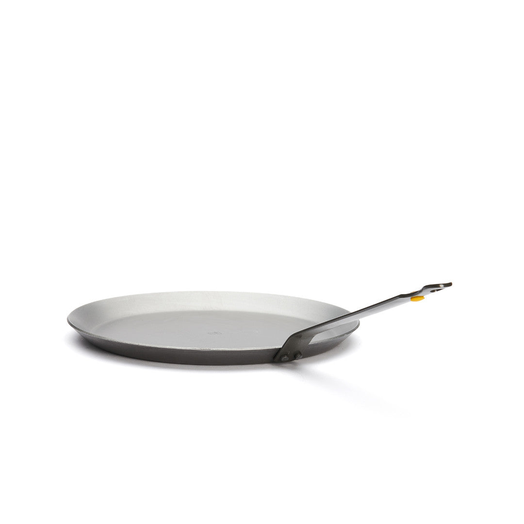 Eine De Buyer Crêpe-Pfanne Mineral B, 26 cm Dm, in flacher, runder Form mit langem, abgewinkeltem Henkel und niedrigem Rand, ist auf weißem Grund fotografiert.
