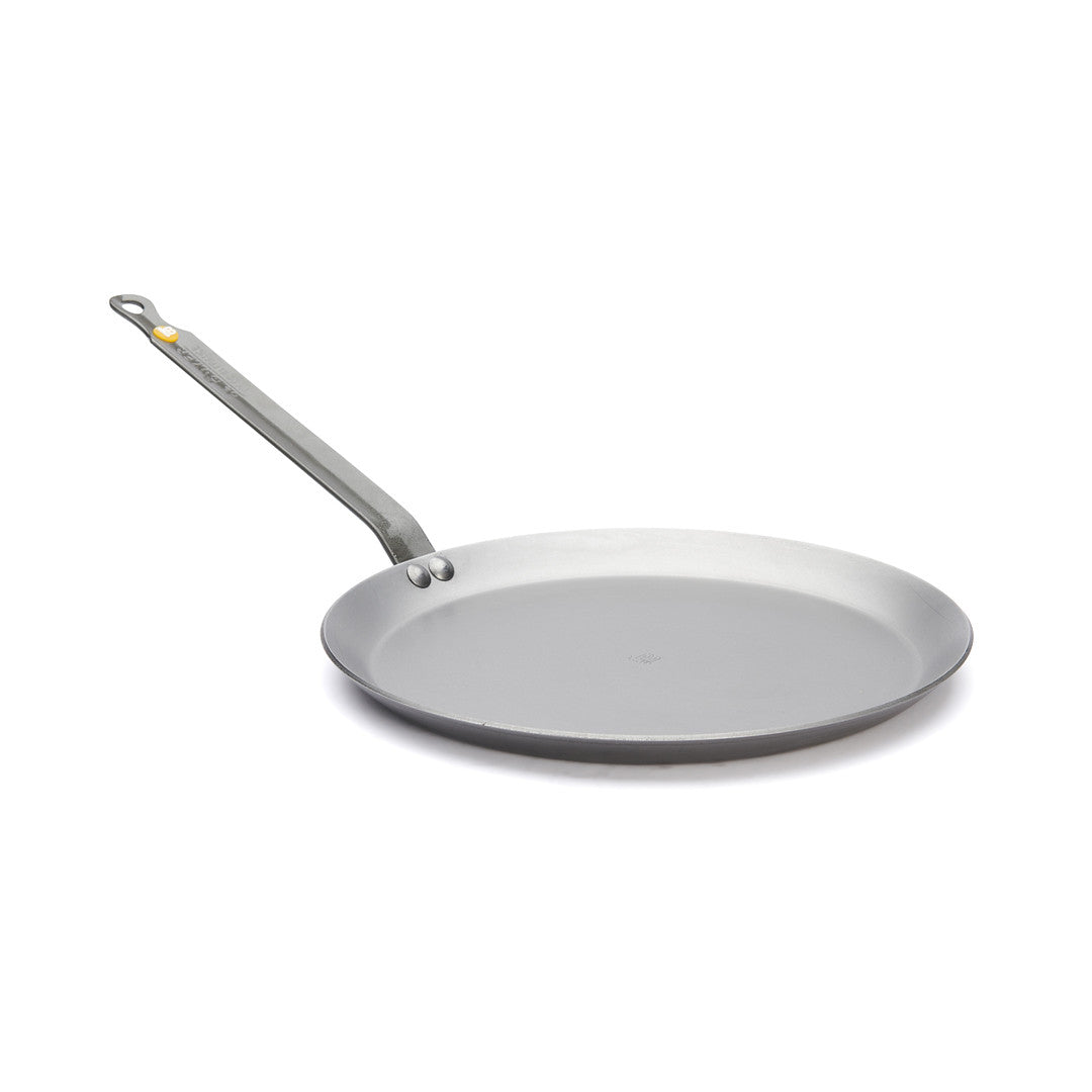 Die De Buyer Crêpe-Pfanne Mineral B, 26 cm Dm, ist eine flache, runde, graue Pfanne mit einem langen Griff und einem Loch am Ende zum Aufhängen. Sie hat eine glatte Oberfläche und ist vor einem weißen Hintergrund abgebildet.