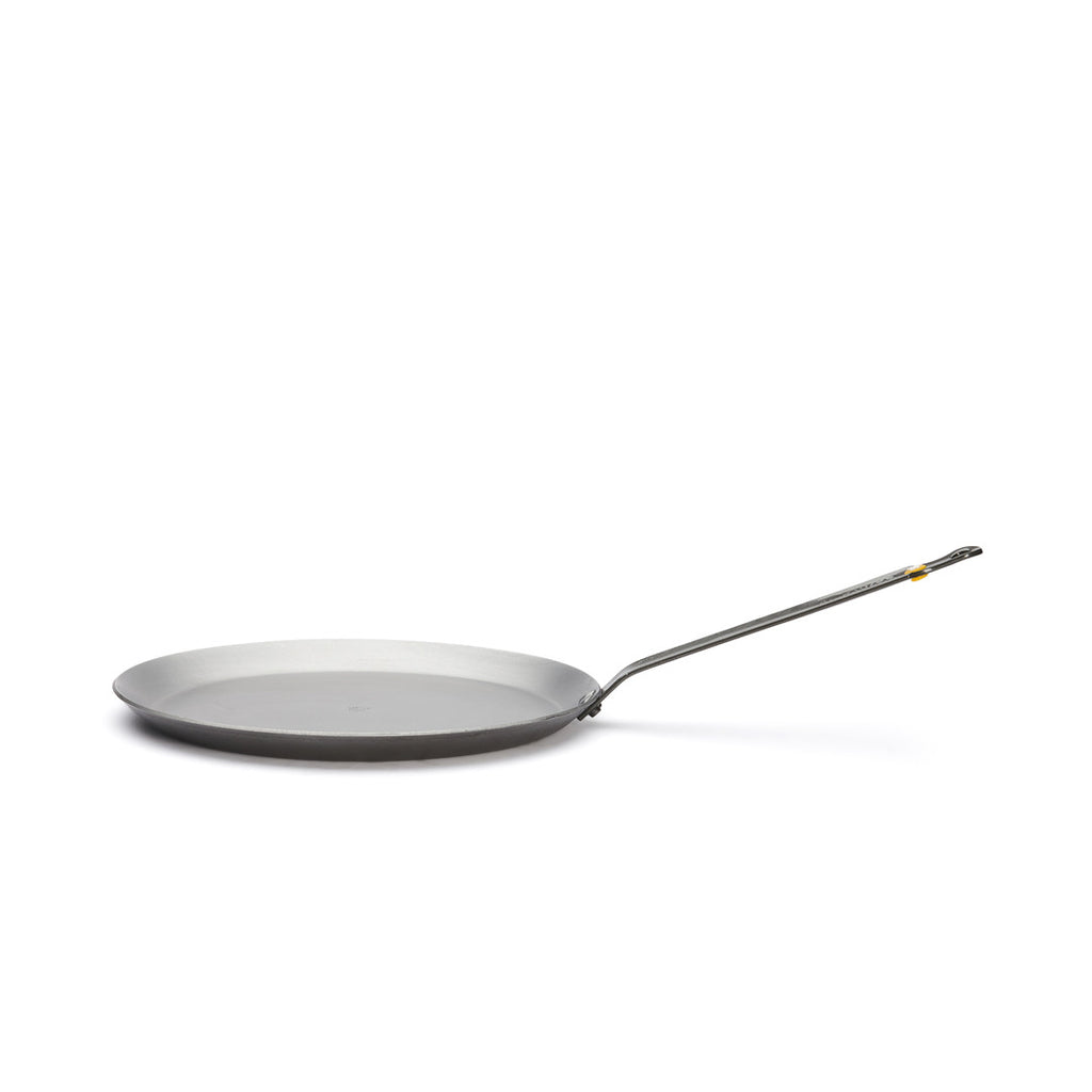 Die De Buyer Crêpe-Pfanne Mineral B, 26 cm Dm, ist eine flache, runde, silberfarbene Pfanne mit einem langen, geraden Metallgriff auf weißem Grund.