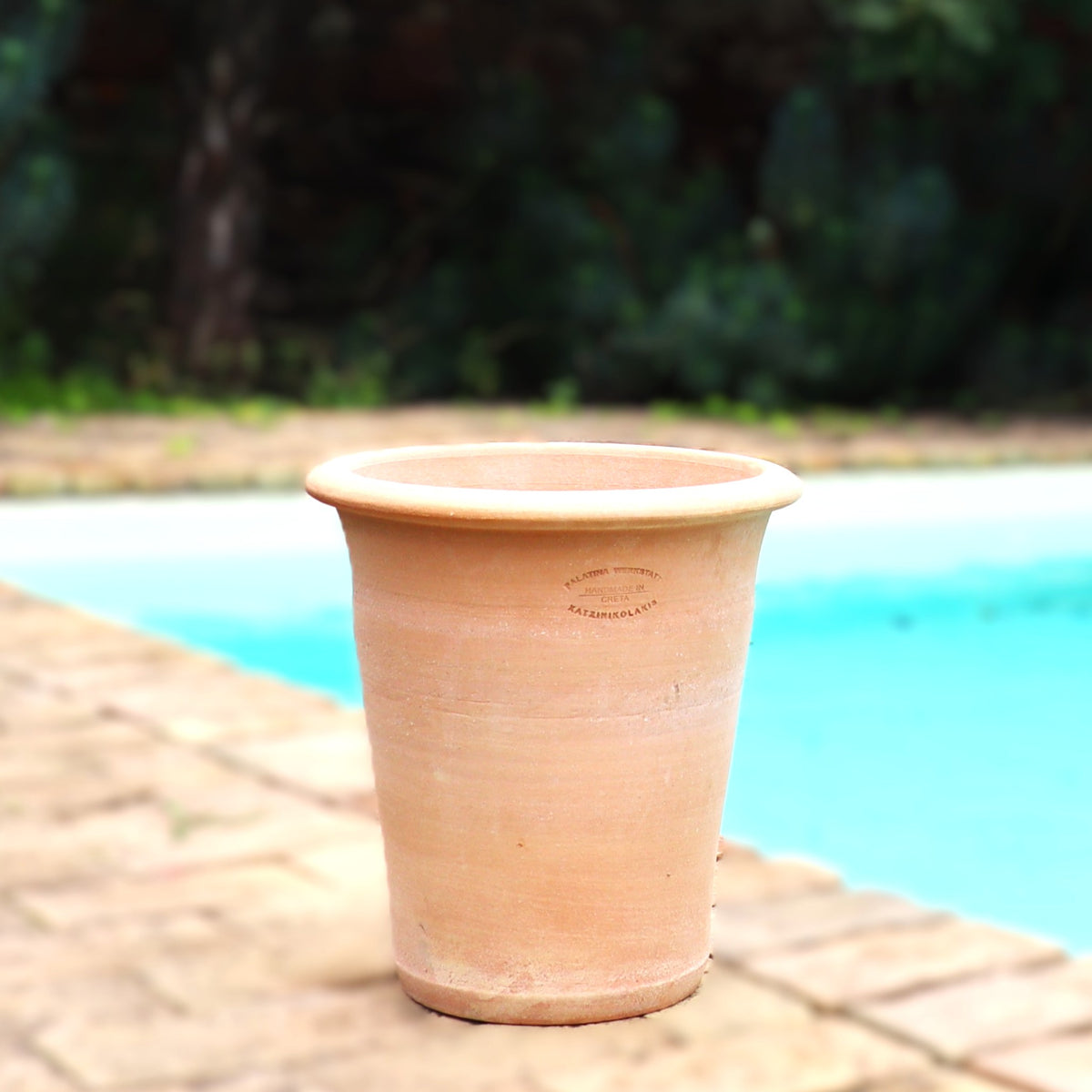 Ein leerer Terrakotta Pflanztopf "Dahlia" 35 cm - handgemacht & frostfest - steht auf einer Steinterrasse neben einem Pool, im Hintergrund verschwimmt grünes Laub.
