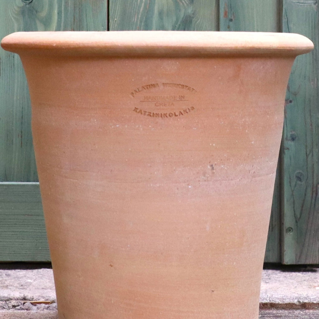 Ein großer Terrakotta-Pflanztopf "Dahlia" 35 cm - Handgemacht & Frostfest mit breitem Rand steht vor grünen Holztüren und weist einen schwachen gestempelten Text in der Nähe des oberen Randes auf, der ihn als in Kreta von Katsarolakis handgefertigt ausweist.