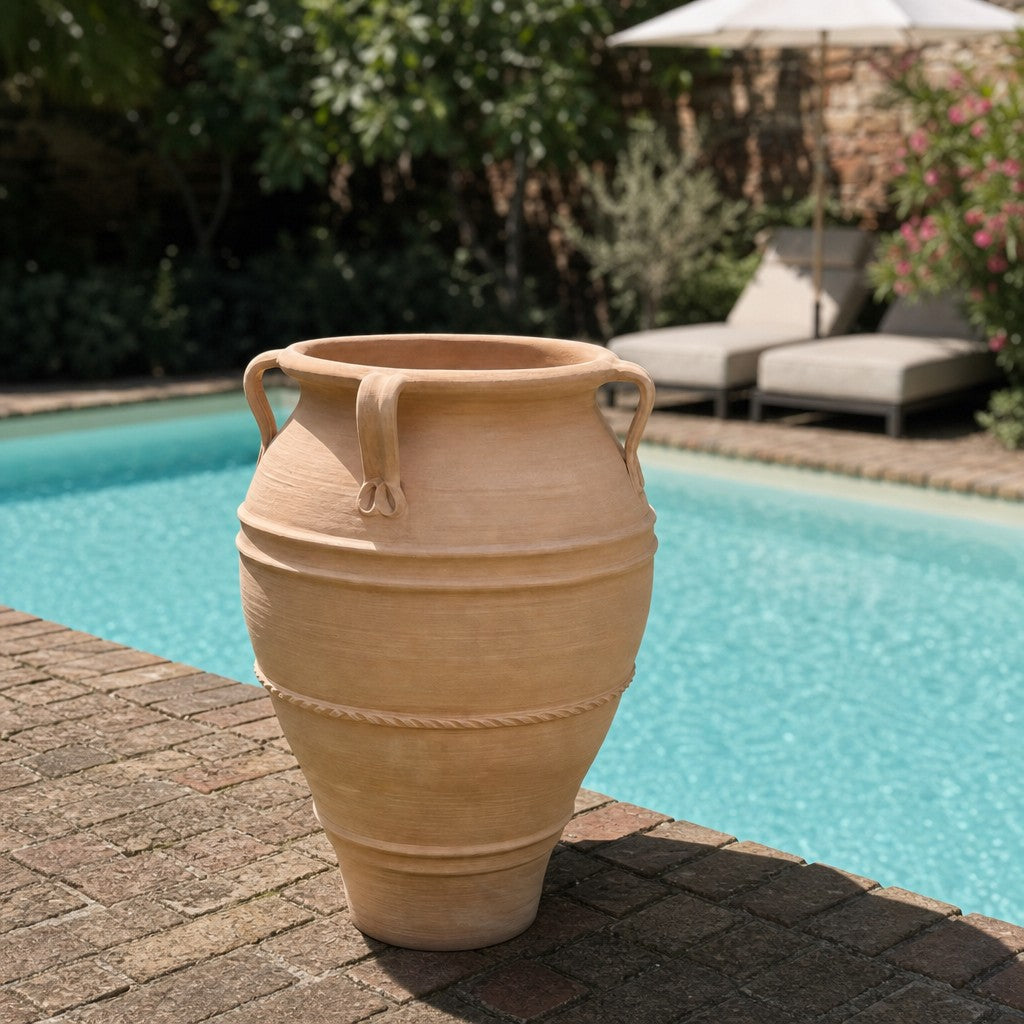 Eine XXL-Amphore aus Terrakotta, die „Datura“ mit einer Höhe von 100 cm und dekorativen Henkeln, steht auf einer Terrasse aus Ziegelsteinen neben einem Swimmingpool. Im Hintergrund sind Liegestühle und Grünpflanzen zu sehen.