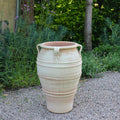 Die frostfeste Terrakotta-Amphore "Datura", H=70 cm, mit zwei seitlichen Griffen und dekorativen Rillen, steht auf einem Kiesweg in einem Garten mit üppigen grünen Pflanzen und Bäumen im Hintergrund.