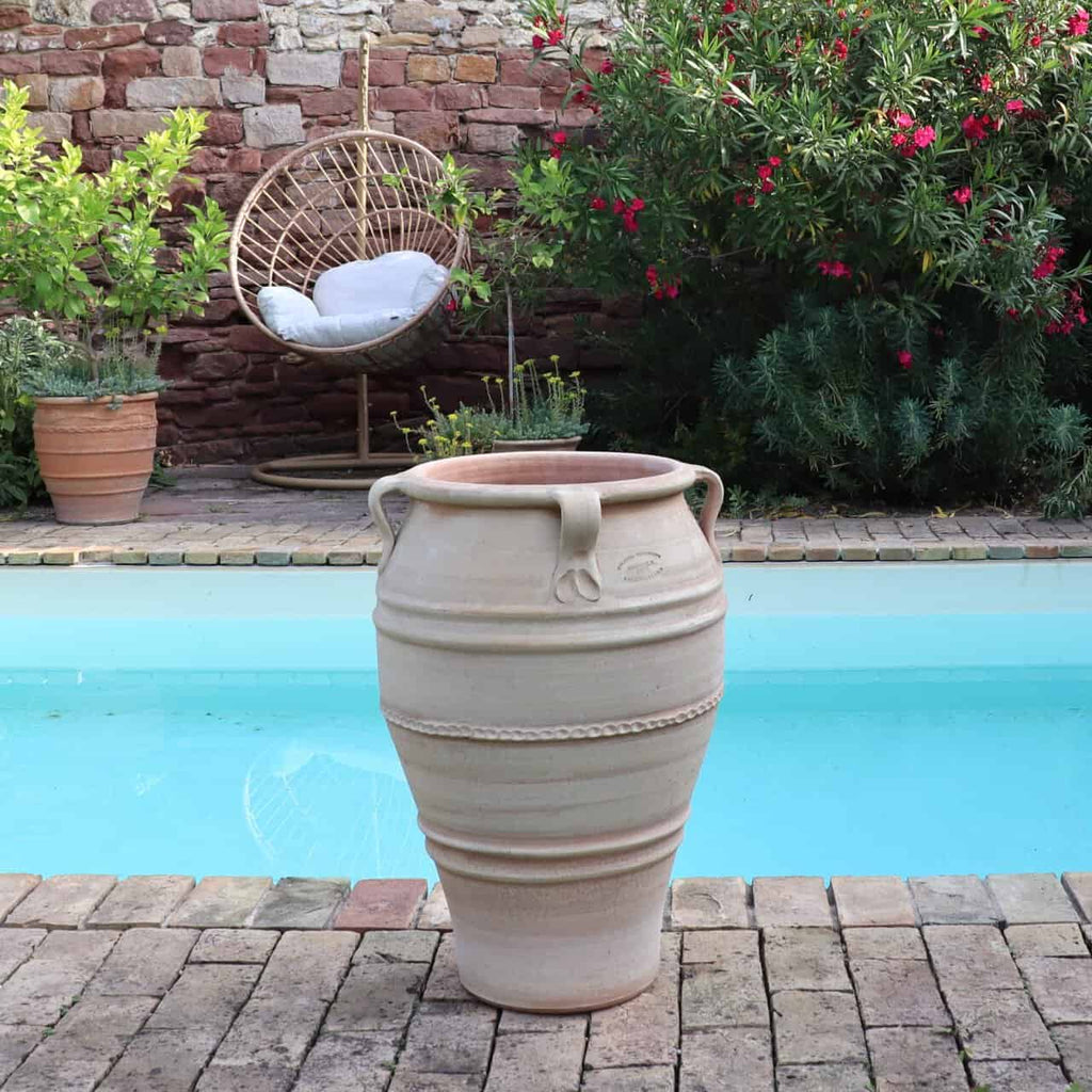 Die frostfeste Terrakotta-Amphore "Datura", H=70 cm, steht auf Backsteinpflaster an einem türkisfarbenen Pool, mit einem Hängesessel und Datura-Topfpflanzen im Hintergrund vor einer Backsteinwand.
