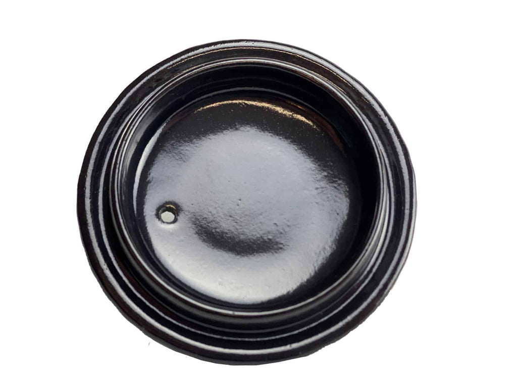 Eine Draufsicht auf einen schwarzen, runden Deckel mit glänzender Oberfläche und Gewinderändern, die an die chinesische Teekanne, Gusskanne, Modell: Yini, erinnern. In der Mitte des Deckels befindet sich ein kleines Loch in der Nähe des Randes. Der kontrastierende weiße Hintergrund lässt den Deckel hervorstechen.