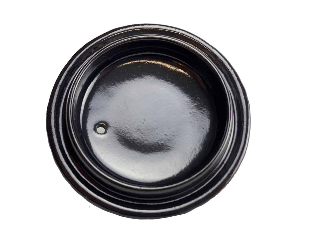 Eine Draufsicht auf einen schwarzen, runden Deckel mit glänzender Oberfläche und Gewinderändern, die an die chinesische Teekanne, Gusskanne, Modell: Yini, erinnern. In der Mitte des Deckels befindet sich ein kleines Loch in der Nähe des Randes. Der kontrastierende weiße Hintergrund lässt den Deckel hervorstechen.