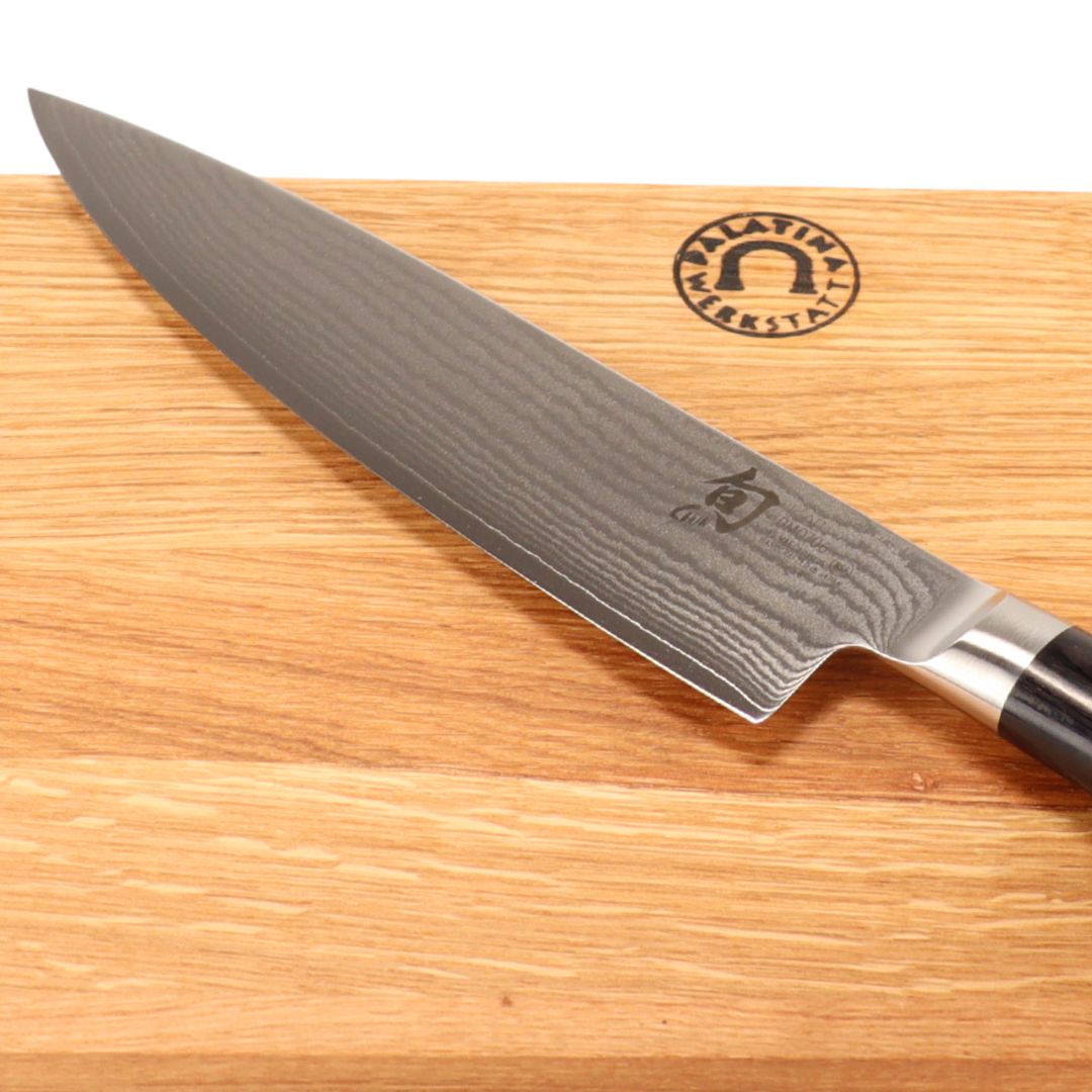 Ein Kai Shun Classic DM-0706 Kochmesser 20 cm mit dunklem Griff liegt auf einem 30x20 cm Schneidebrett aus Eichenholz, das oben rechts ein rundes Logo mit Text trägt.