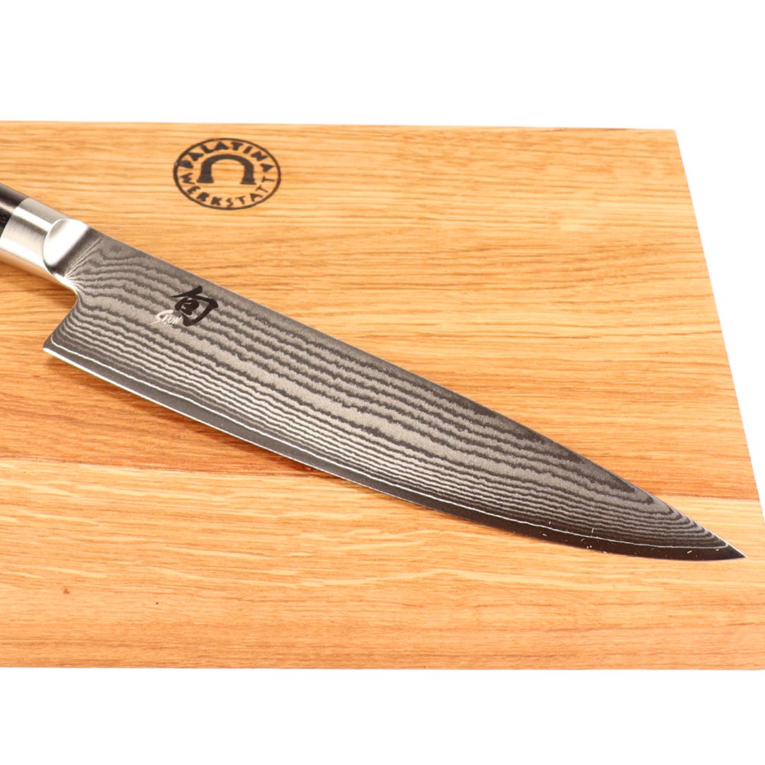 Ein Kai Shun Classic DM-0706 Kochmesser mit 20 cm Klinge liegt auf einem 30x20 cm Schneidebrett aus Eichenholz, das mit einem runden Logo graviert ist.