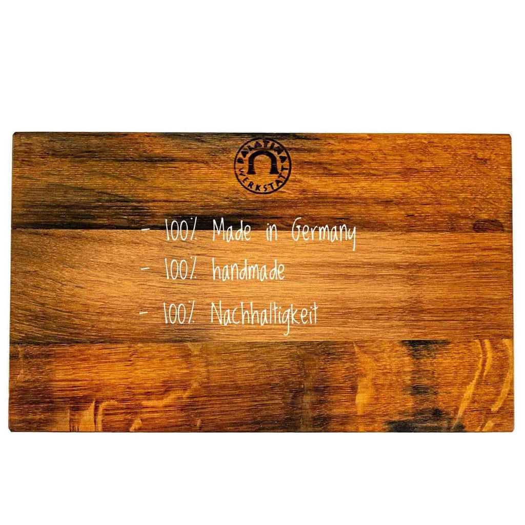 Ein Schneidebrett aus Holz mit weißem Text darauf. Der Text lautet: „100 % Made in Germany“, „100 % handgefertigt“ und „100 % Nachhaltigkeit“. Das Schneidebrett hat oben in der Mitte ein Logo oder Markenzeichen. Das Holz hat eine satte, mehrfarbige Oberfläche.