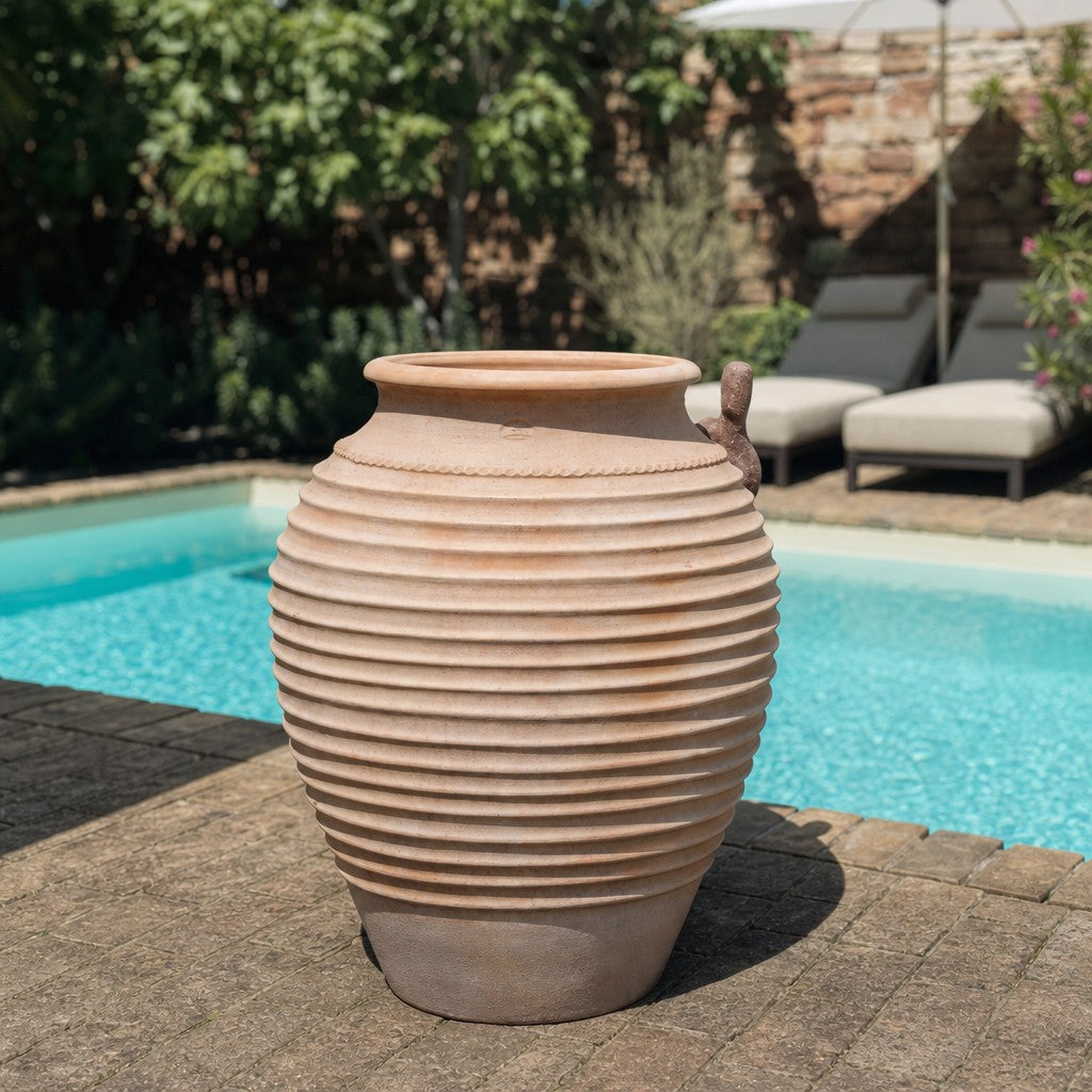 Ein großer, gerippter Tontopf – ähnlich einer Winterharte-Dekorationsamphore „Ficus“, H=100 cm – steht an einem sonnigen Tag auf einer Steinterrasse neben einem türkisfarbenen Swimmingpool, im Hintergrund sind Liegestühle und Grünpflanzen zu sehen.