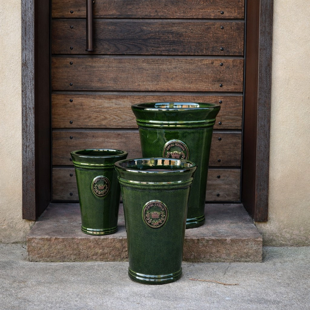 Drei Pflanzkübel der Serie „Vasenform“ in der Farbe „Garden Green“ mit einer Höhe von 33–51 cm aus grüner Keramik mit kreisförmigen Emblemen stehen auf einer Steinstufe vor einer Holztür.