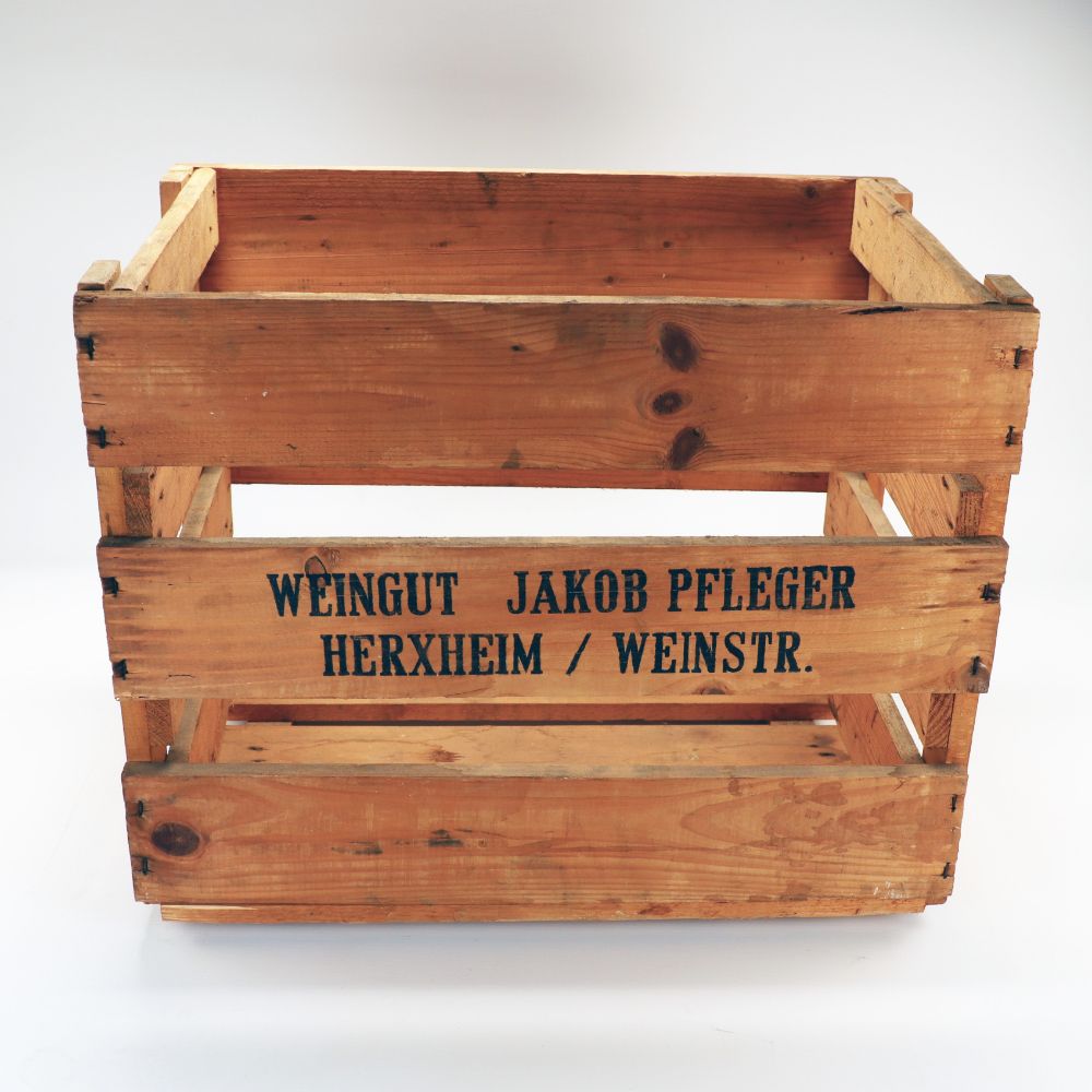 Eine Vielseitige Weinkiste im Vintage-Look, 48x32x38 cm groß, mit Lamellenwänden und ohne Deckel, trägt auf der Vorderseite den schwarzen Text „WEINGUT JAKOB PFLEGER HERXHEIM / WEINSTR.“ Diese rustikale Kiste steht auf weißem Untergrund und eignet sich perfekt als Regal, Schuhregal oder Dekoelement.