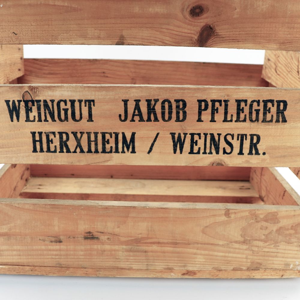 Eine vielseitig einsetzbare Weinkiste aus Holz im Vintage-Look mit dem Text „Weingut Jakob Pfleger Herxheim / Weinstr.“ Die Kiste mit ihrer rustikalen Oberfläche und den sichtbaren Holzmaserungen und Ästen verleiht ihr einen majestätischen Charme und eignet sich perfekt als Regal, Schuhregal oder Dekorationselement. Maße: 48x32x38 cm.