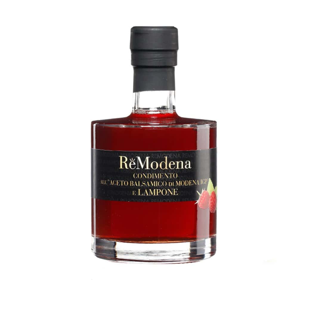 Eine Flasche Aceto Balsamico Essig di Modena I.G.P. 250 ml in verschiedenen Sorten, mit zylindrischer Form und klarem Glaskörper. Die tiefrote Flüssigkeit ist durch das Glas sichtbar. Das schwarze Etikett zeigt den Produktnamen und hat unten rechts Bilder von Himbeeren, die die Herkunft des Aceto Balsamico di Modena Bio zeigen.