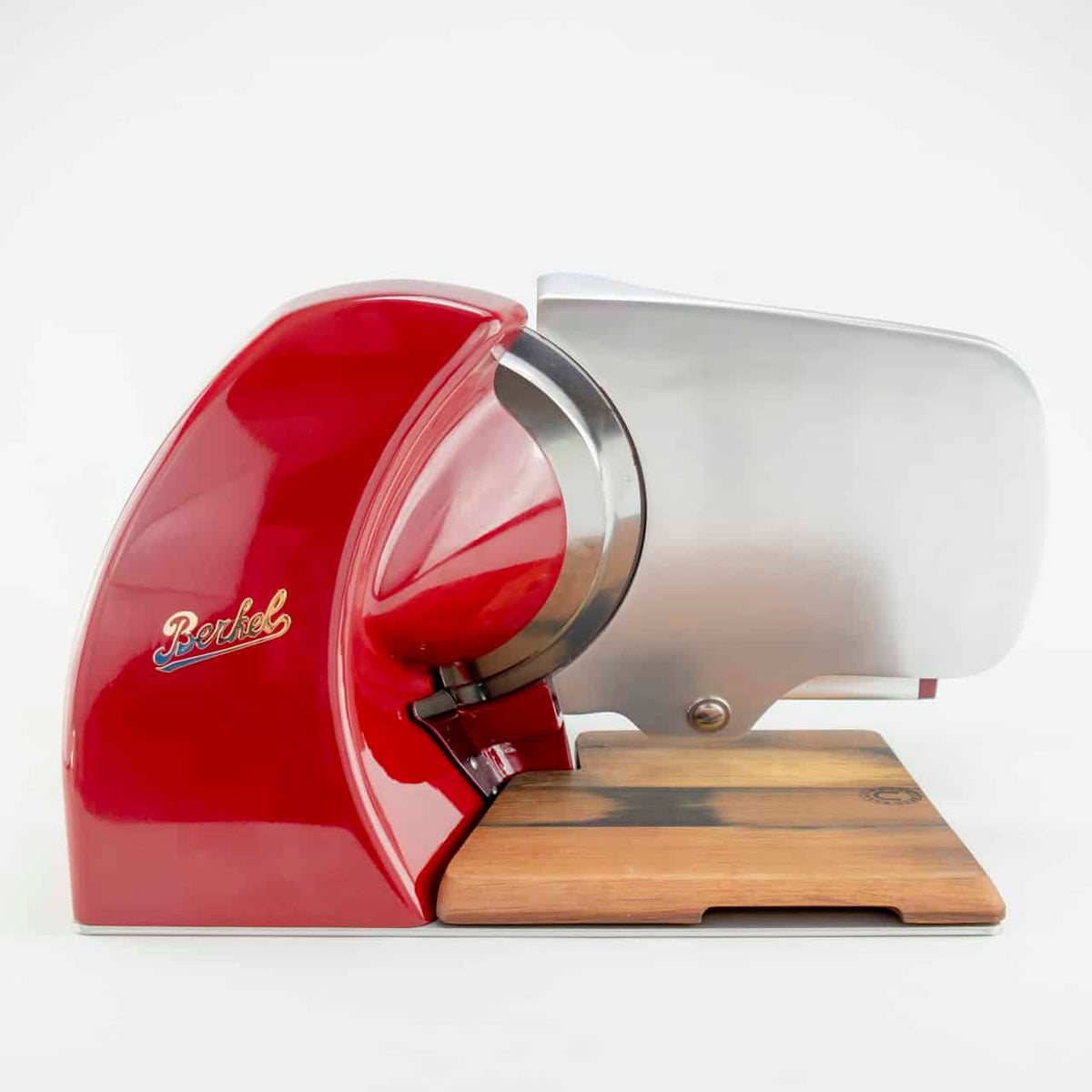 Eine Berkel Home Line 250 Rot, Aufschnittmaschine + von Hand gefertigtes Fassholzbrett aus alten Weinfässern steht auf einer hellen Holzfläche. Der Aufschnitter verfügt über eine metallisch glänzende Klinge und ein schlankes, kompaktes Design. Auf dem roten Gehäuse ist der Markenname „Berkel“ zu sehen. Der Hintergrund ist schlicht weiß.