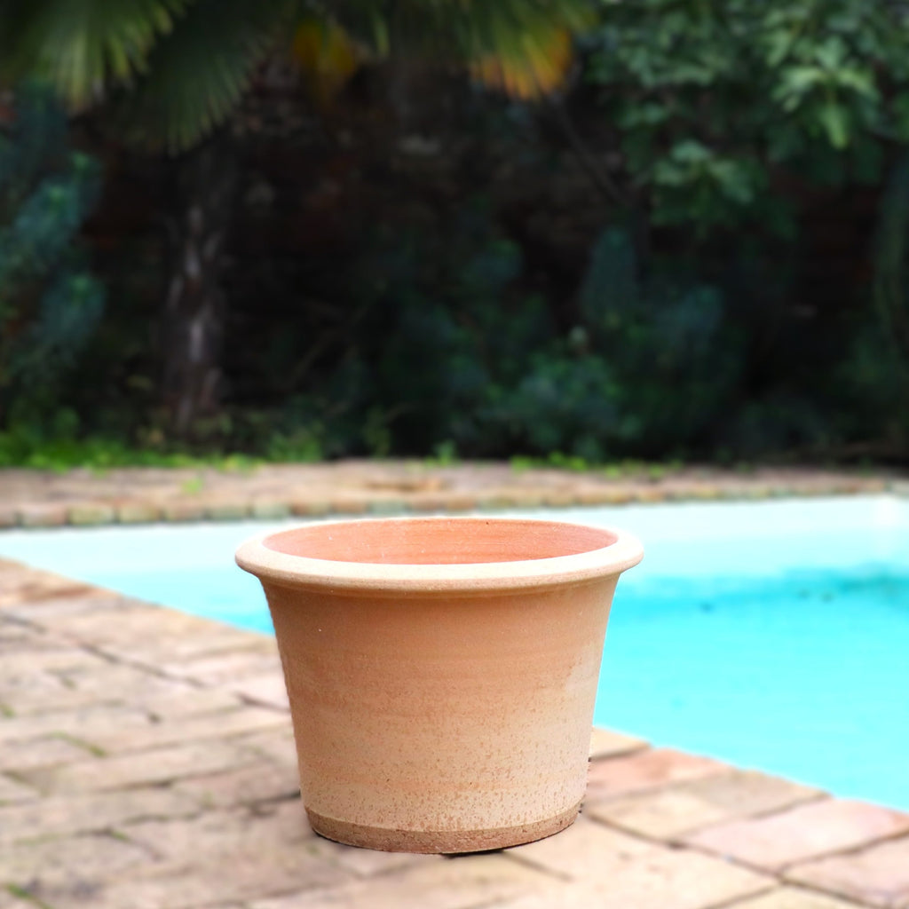 Der Terrakotta Pflanztopf "Hosta" 35 cm - handgemacht & frostfest, mit Ablaufloch, steht leer auf einer Backstein-Terrasse am Pool, im Hintergrund verschwimmt grünes Blattwerk.