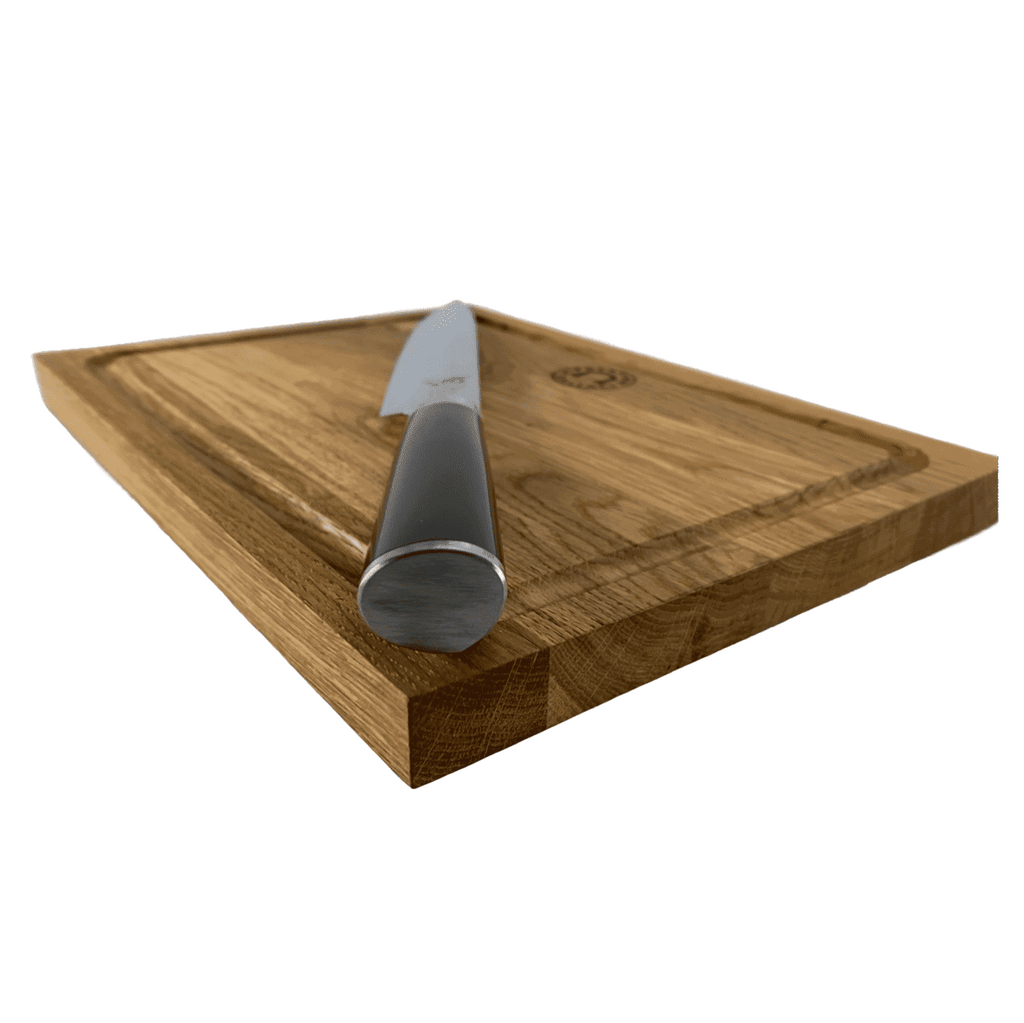 Ein Kai Shun Classic DM-0704 Schinkenmesser mit einer 23 cm langen Damastklinge ruht diagonal auf einem 30 x 22 cm großen Eichenschneidebrett. Das Schneidebrett weist eine Rille an den Kanten auf und weist eine natürliche Holzmaserung auf. Das Bild wurde aus einem niedrigen Winkel aufgenommen und konzentriert sich auf den Messergriff.