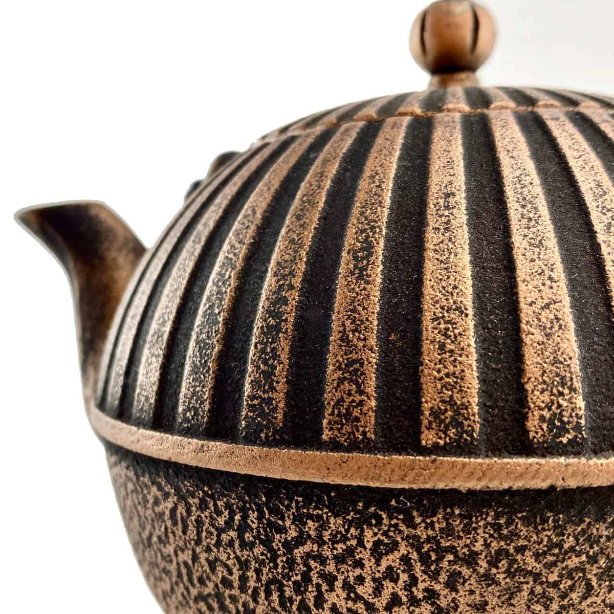 Nahaufnahme der chinesischen Teekanne aus Keramik, Modell: Yini, mit geriffeltem, strukturiertem Design in einer auffälligen Mischung aus dunkelbraunen und beigen Farben. Der teilweise sichtbare Deckel hat oben einen kleinen runden Griff. Der Ausguss und ein Teil des Griffs sind ebenfalls zu sehen.