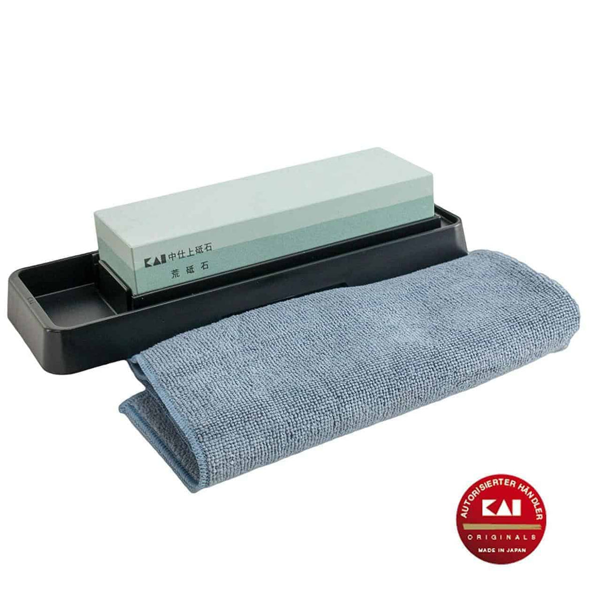 Ein rechteckiger Kai AP-0305 Schleifstein | Wetzstein Messerschärfer 400/1000 Körnung mit schwarzer Basis, daneben liegt ein gefaltetes blaues Poliertuch. Der Schleifstein trägt japanische Inschriften und in der unteren rechten Ecke befindet sich ein roter runder Aufkleber mit der Aufschrift „KAI“ und „Made in Japan“.