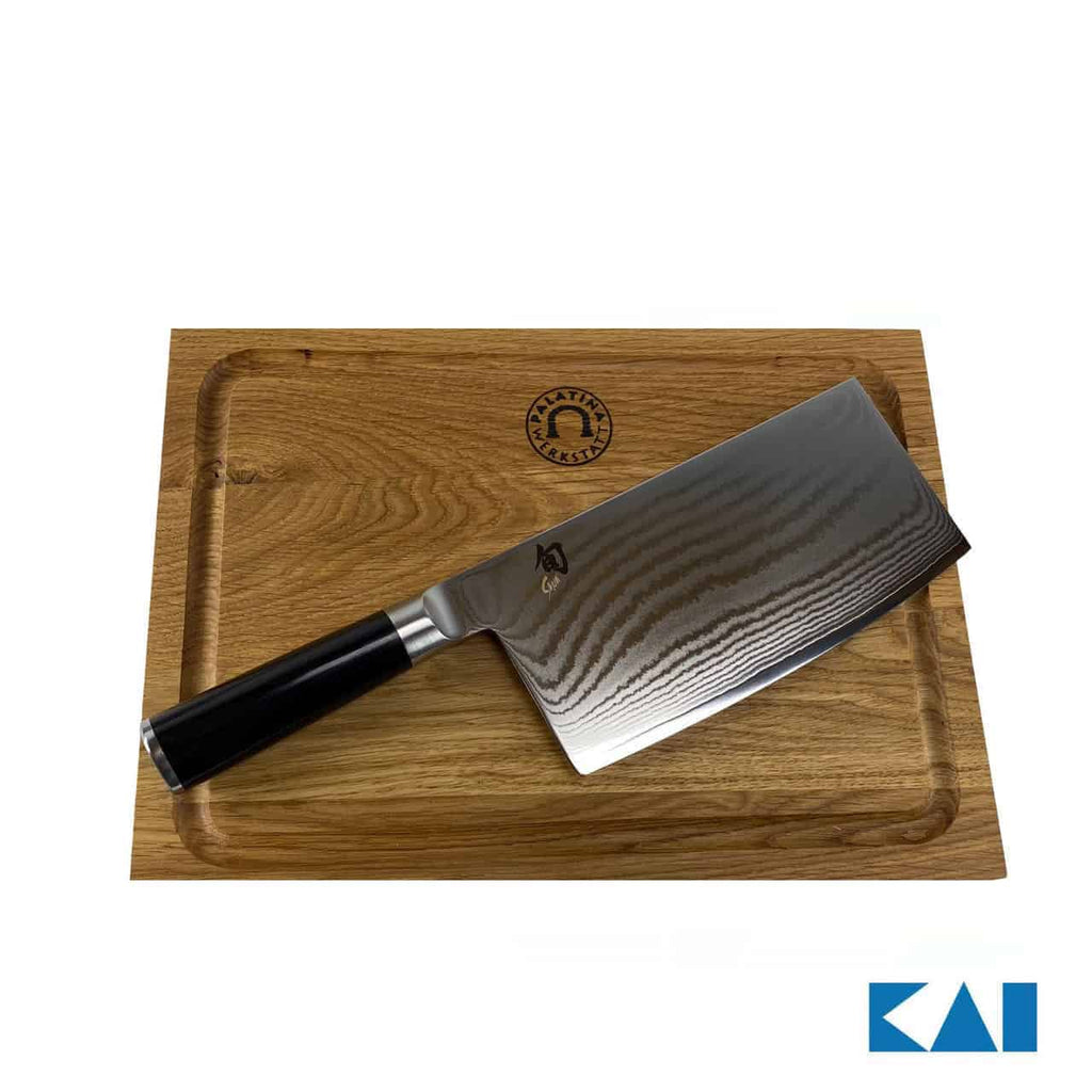 Ein hochwertiges Kai Shun Classic Chinakochmesser DM-0712 mit glänzender Stahlklinge und schwarzem Griff ruht auf einem 30x22 cm großen Schneidebrett aus Eiche. Das Schneidebrett hat eine Rille um die Kanten und ein kleines Logo in der oberen Mitte. Das KAI DM-0712-Logo erscheint in der unteren rechten Ecke.