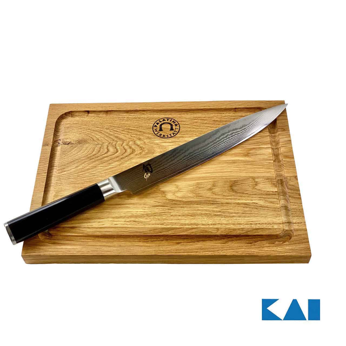 Ein langes, schlankes Kai Shun Classic DM-0704 Schinkenmesser mit schwarzem Griff liegt auf einem hölzernen Schneidebrett von 30 x 22 cm mit geschnitzten Kanten. Das Schneidebrett weist oben in der Mitte ein Emblem auf. Die 23 cm lange Damastklinge des Messers glänzt im Licht und das KAI-Logo ist in der unteren rechten Ecke des Bildes sichtbar.