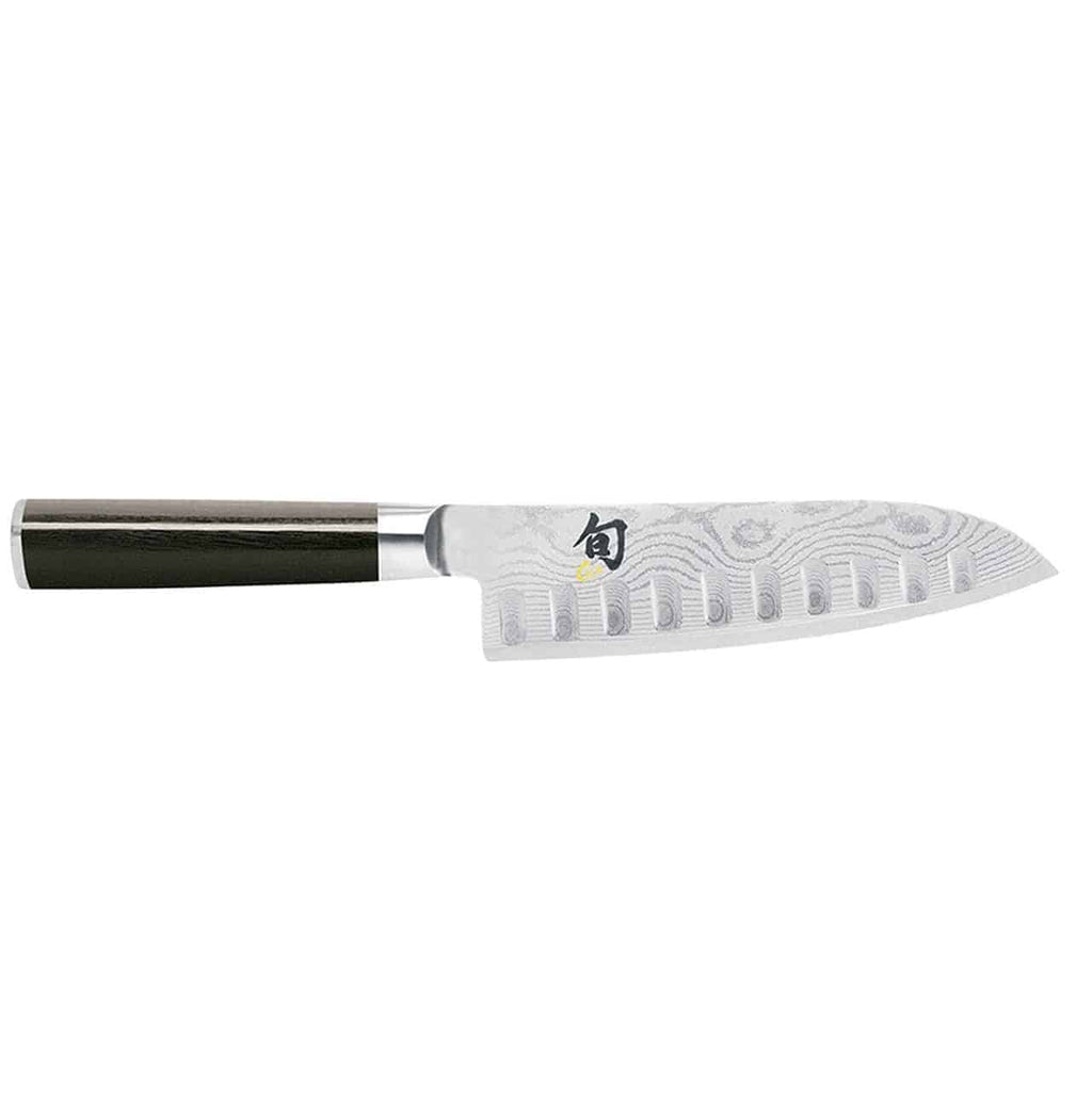 Das Kai Shun Classic Santoku DM-0718 ist ein professionelles Kochmesser mit schwarzem Griff und 18 cm langer silberner Klinge mit markanten Kullenschliff-Einkerbungen. Die Klinge hat eine einzigartige Textur und ist in der Nähe des Griffs mit einem kleinen, farbenfrohen Logo versehen. Es wird außerdem mit einem 34 x 21 cm großen Fassholzbrett geliefert.