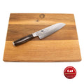 Ein Kai Shun Tim Mälzer TDM-1702 Santokumesser mit 18 cm langer Damaszenerstahlklinge und dunklem Griff ruht diagonal auf einem 40x30 cm großen Küchenarbeitsbrett aus Holz. Die Logos des Schneidebrettherstellers und des Messerherstellers sind deutlich zu erkennen. Das Santokumesser trägt die Aufschrift „Kai Original“ und „Made in Japan“.