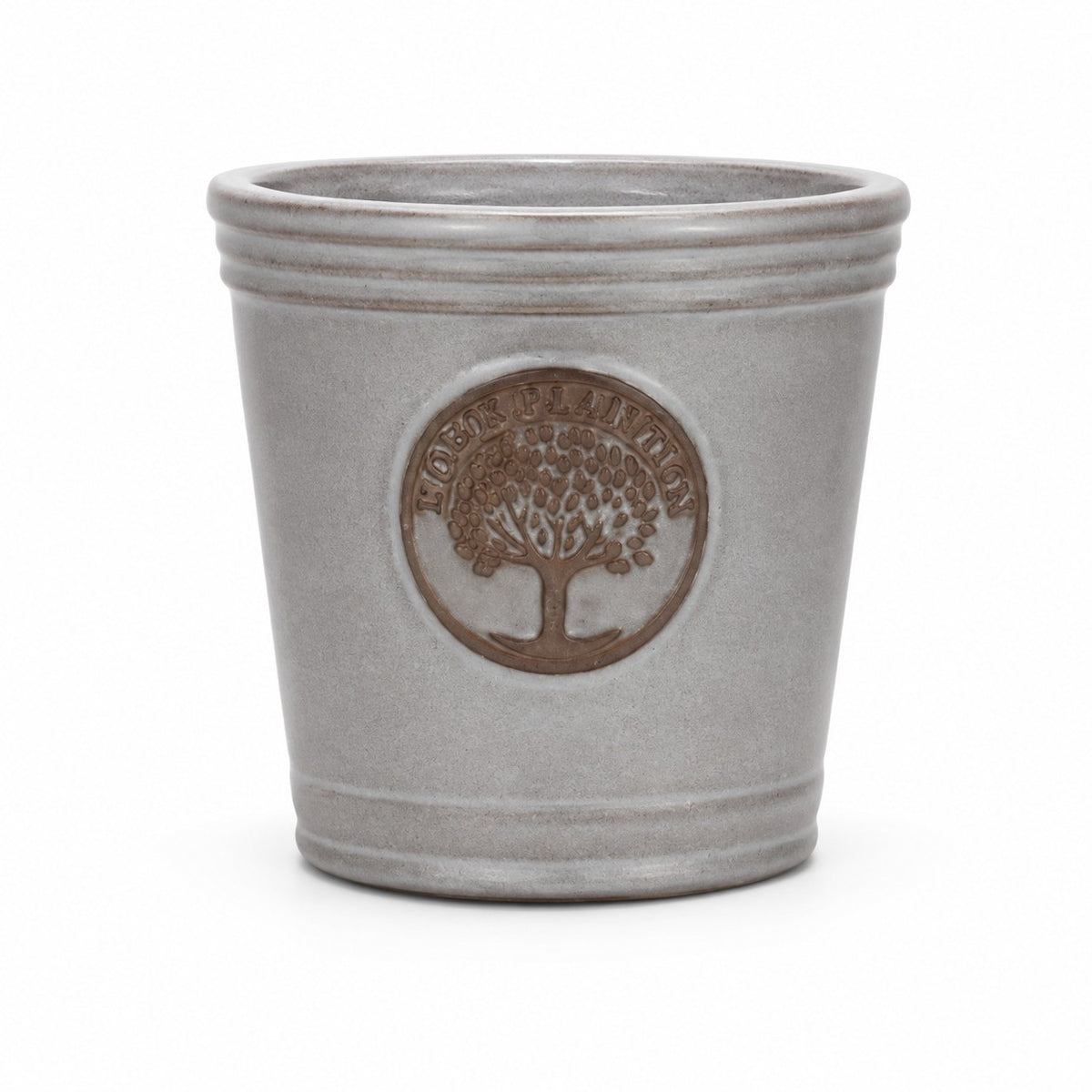 Ein kleiner, glasierter Pflanzkübel „Cappuccino“ (Höhe 15–24 cm) in Grau mit rundem Emblem und Baummotiv sowie „Flora Planting“-Prägung. Er besticht durch schlichtes Design, zwei Rillen am Rand und einen dezenten metallischen Glanz.