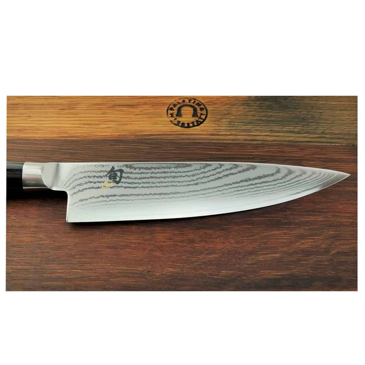 Eine Nahaufnahme des hochwertigen Kai Shun Classic DM-0706 Kochmessers mit einer 20 cm langen Klinge aus Damaszenerstahl mit aufwendigen Wellenmustern. Das Messer ist auf einem hölzernen Schneidebrett aus Fassholz mit den Maßen 30 x 18 cm platziert, mit einem runden schwarzen Logo in der oberen Mitte, das eine stilisierte Kochmütze und den Text „Sharp Cutlery“ zeigt.