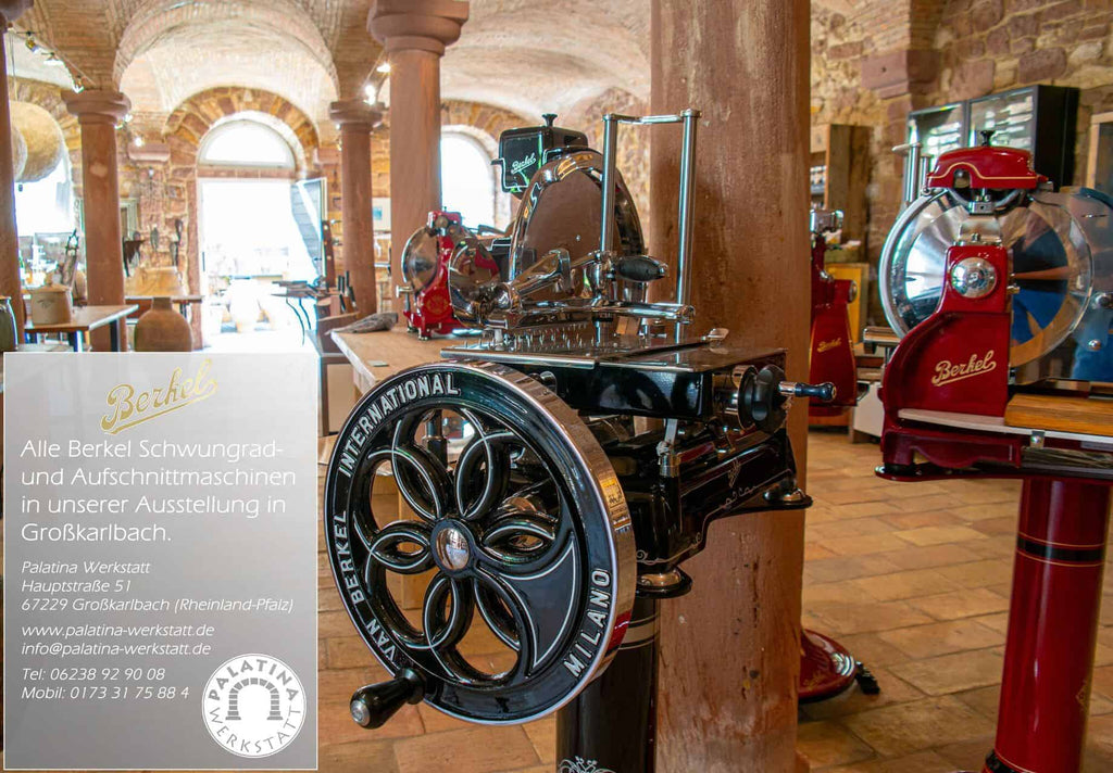 In einem gut beleuchteten Raum mit Bogenfenster und Steinwänden steht eine alte Aufschnittmaschine von Berkel. Ein Schild in der Nähe weist auf die Berkel Red Line 300 Schwarz hin, eine Original Profi-Aufschnittmaschine mit einem Messerdurchmesser von 300 mm, komplett mit Fassholz-Einlegebrett, erhältlich bei der Palatina Werkstatt in Großkarlbach, Deutschland.