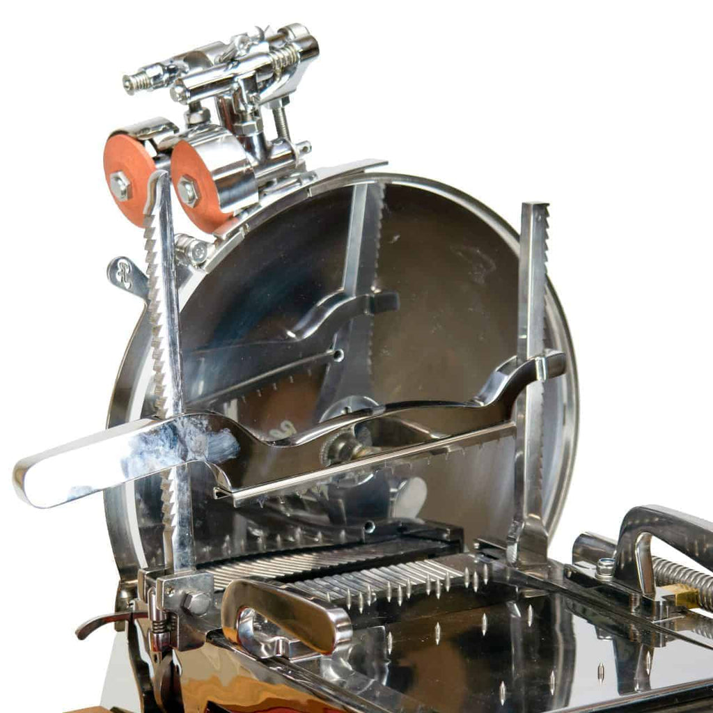Eine Nahaufnahme einer nostalgischen Berkel Volano L16 Schwungrad-Aufschnittmaschine mit runder Klinge, Metallteilen und Einstellknöpfen. Die Aufschnittmaschine hat eine glänzende silberne Oberfläche und verschiedene Komponenten zum Halten und Schneiden verschiedener Fleischsorten. Oben sind rote runde Elemente sowie ein handgefertigtes Schneidebrett zu sehen.