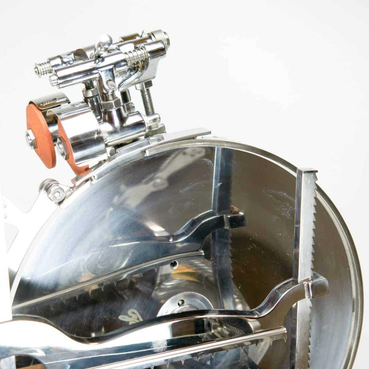 Nahaufnahme eines glänzenden Kreissägeblatts aus Metall mit komplizierten Komponenten und einem roten Aufsatz oben, der an die nostalgische Berkel Volano L16 Schwungrad Aufschnittmaschine rot + handgefertigtem Einlegebrett erinnert. Die Zähne des Blatts sind deutlich sichtbar und die Gesamtoberfläche ist poliert und reflektiert das Licht.