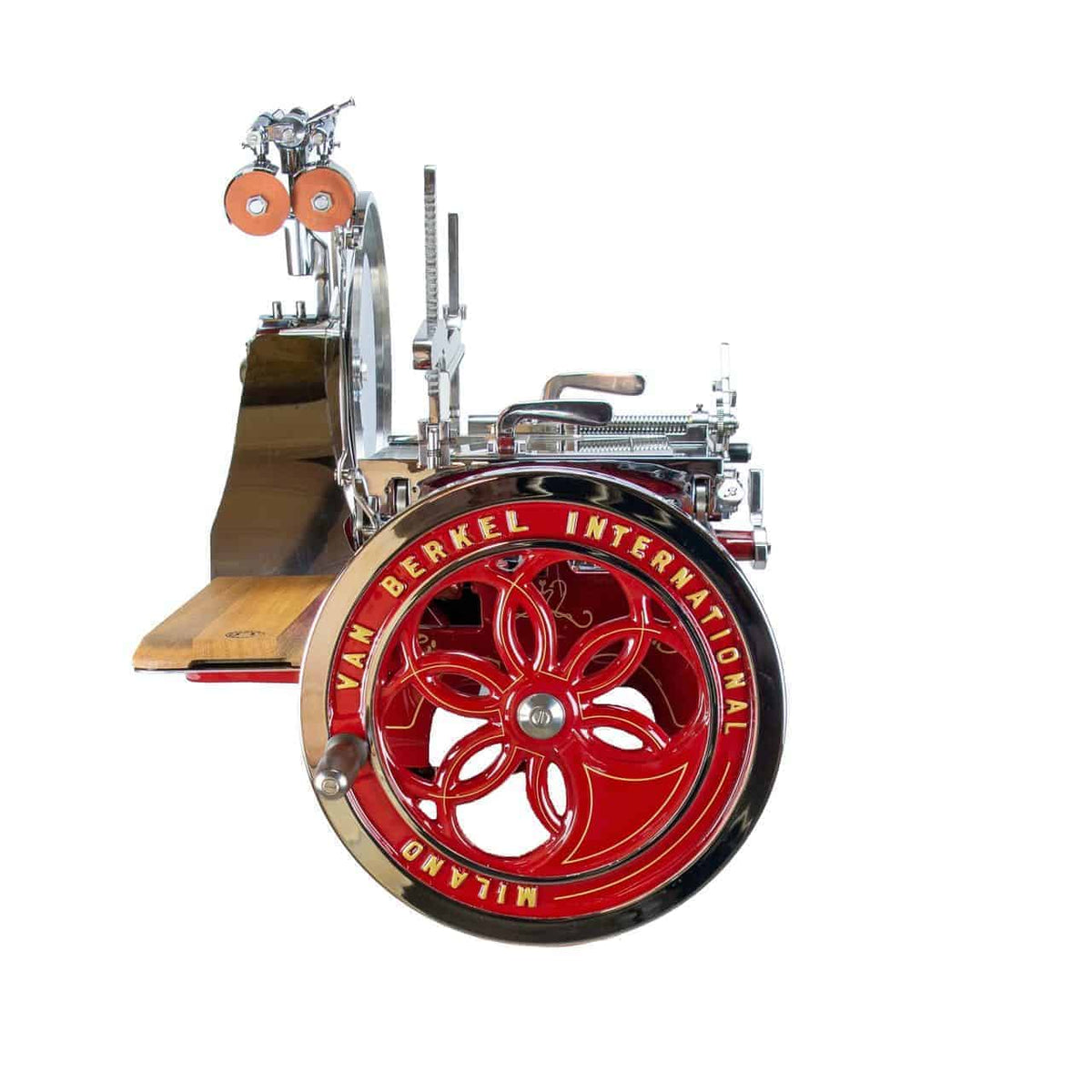 Eine nostalgische Schwungrad-Aufschnittmaschine vom Typ Berkel Volano L16 in einem auffälligen Rotton, mit einem großen runden Rad mit komplizierten Metallkomponenten und dekorativen Speichen, die mit goldener Beschriftung geschmückt sind, steht stolz auf ihrem handgefertigten Einlegebrett.
