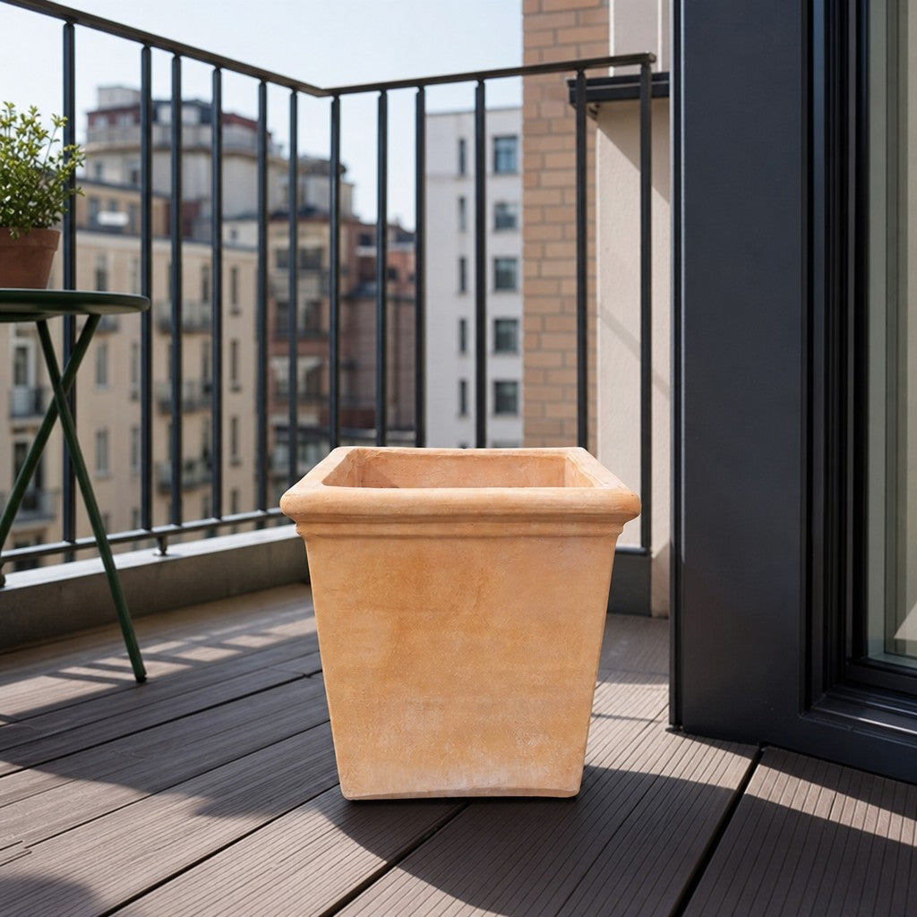 Ein großer, leerer Terrakotta-Blumenkübel steht auf einem Holzbalkon mit schwarzem Metallgeländer und bietet an einem sonnigen Tag einen Blick auf die Gebäude der Stadt.