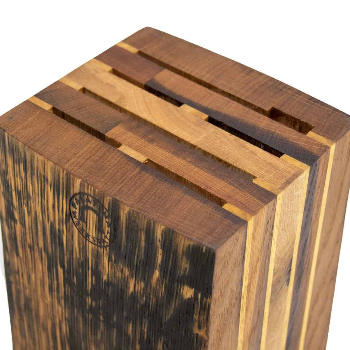 Eine Nahaufnahme des exklusiven Messerblocks, der aus den Dauben alter Eichenweinfässer gefertigt wurde und mehrere Schlitze für verschiedene Küchenmesser hat. Der Block weist eine Mischung aus dunklen und hellen Holztönen auf und zeigt eine rustikale Ästhetik. Auf einer Seite des Blocks ist ein kreisförmiges Logo eingraviert.