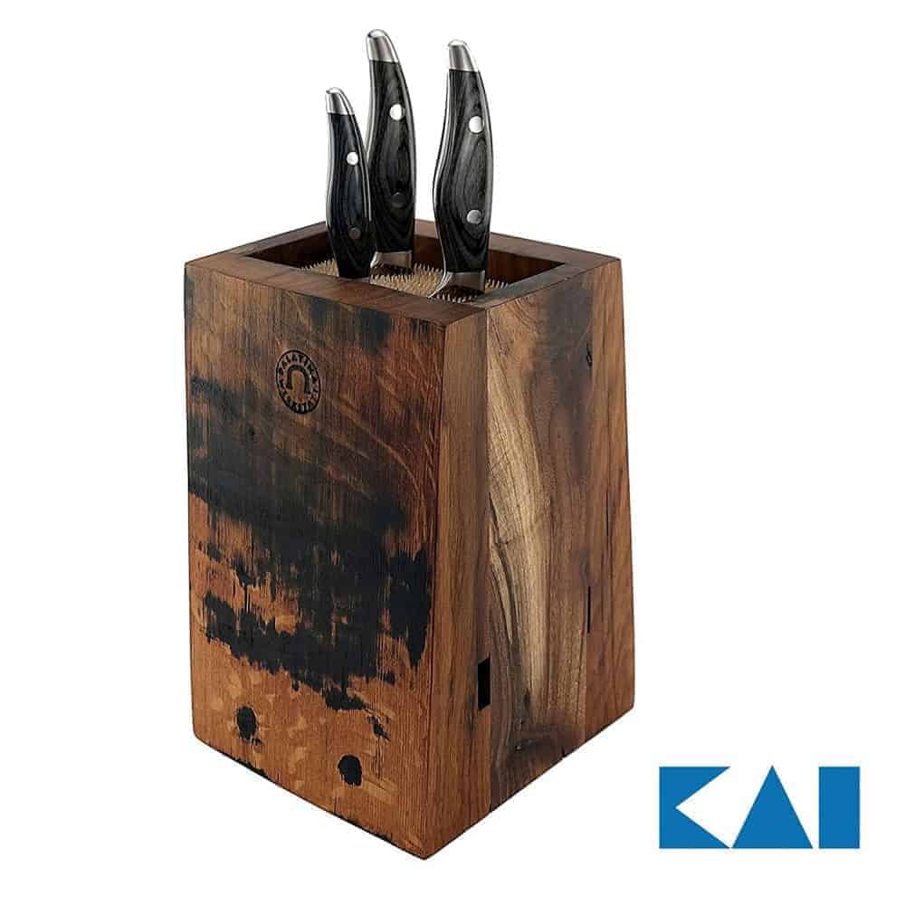 Ein Messerblock aus Fassholz mit drei Kai Shun Nagare-Messern (NDC-0700-0702-0705) mit schwarzen Griffen und teilweise gebranntem Holzfinish. Der Block trägt in der unteren rechten Ecke das Markenlogo „Kai“, das die Eleganz der Kai Shun Nagare-Serie unterstreicht.