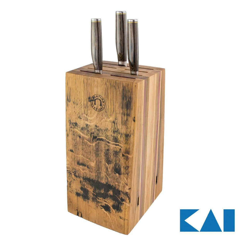 Ein handgefertigter Messerblock aus Holz von Alten Fassdauben, der drei Kai Shun Premier Tim Mälzer Profimesser mit Metallgriffen hält, ist auf weißem Hintergrund abgebildet. Der Block weist ein abgenutztes, altmodisches Aussehen mit dunklen Flecken und Kratzern auf, die an alte Fassdauben erinnern. Das Markenlogo „KAI“ ist in der unteren rechten Ecke in Blau und Weiß abgebildet.