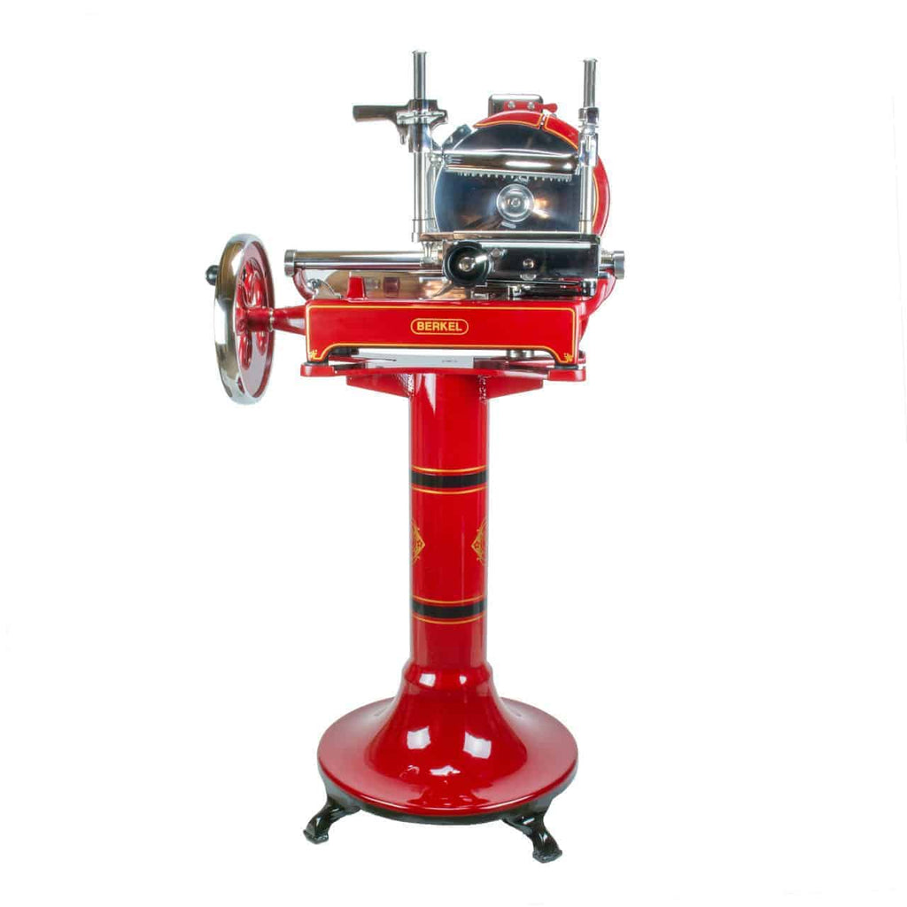 Ein roter Aufschnittschneider im Vintage-Stil mit handbetriebenem Schwungrad, montiert auf einem passenden rot-schwarzen Ständer mit goldenen Akzenten. Die Schneide und die Plattform sind aus poliertem Metall und der Markenname „Berkel“ ist deutlich auf dieser exquisiten Berkel Volano P15 Rot Aufschnittmaschine Schwungrad plus Standfuß plus Aufschnittbrett zu sehen.