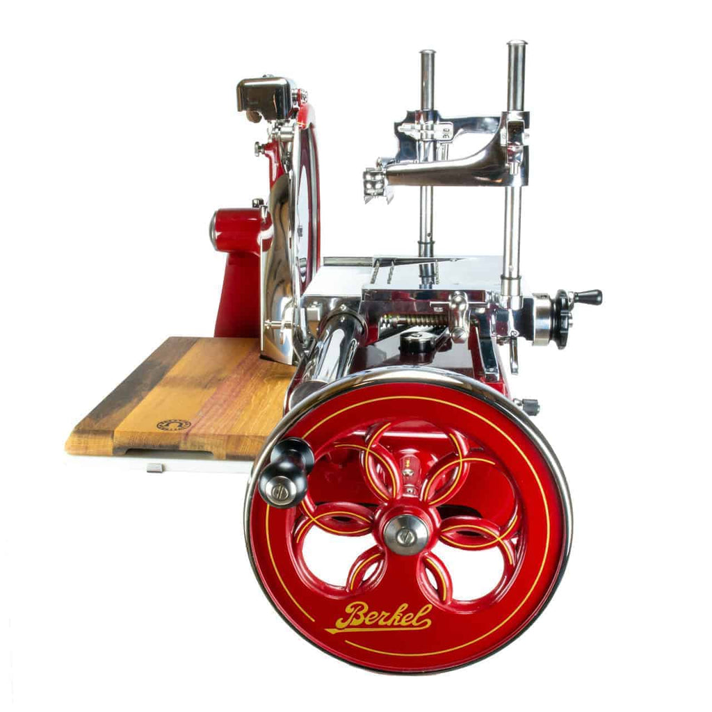 Die Berkel Volano P15 Rot Aufschnittmaschine mit Schwungrad + Einlegebrett verfügt über ein großes vertikales Handrad zum Schneiden von Fleisch und Käse. Diese Aufschnittmaschine im Vintage-Stil in Rot und Chrom besticht durch eine polierte Metallkonstruktion, ein Holzbrett, aufwendige Details und das ikonische Berkel-Logo, das prominent auf dem Handrad angebracht ist.
