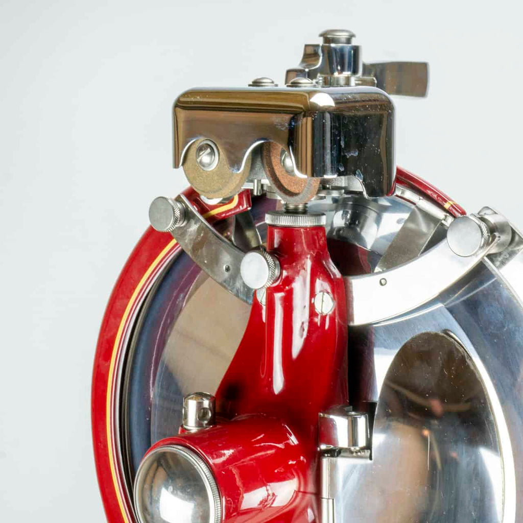 Nahaufnahme einer glänzenden roten und metallischen Aufschnittmaschine Berkel Volano P15 Rot, Schwungrad + Standfuß + Aufschnittbrett mit runder Klinge. Die Aufschnittmaschine verfügt über verschiedene Metallkomponenten, darunter Knöpfe und einen Griff, sowie einen transparenten Schutz, der die Klinge bedeckt. Diese klassische Fleischschneidemaschine ist zum dünnen und gleichmäßigen Schneiden von Fleisch konzipiert.