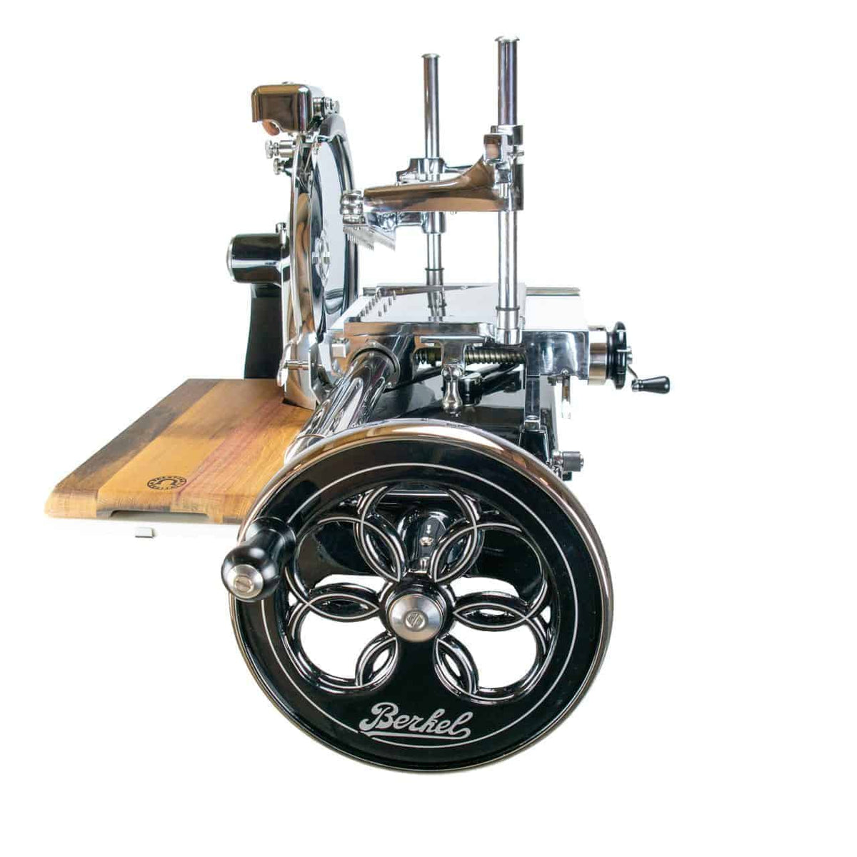 Eine Nahaufnahme des Berkel Volano P15 schwarz, einer manuellen Aufschnittmaschine mit Schwungrad, zeigt seine polierten Metallteile und ein schwarzes Handkurbelrad mit Blumenmuster. Die manuelle Aufschnittmaschine wird mit einem am Metallrahmen befestigten Holzschneidebrett geliefert, was ihre komplizierten Details und klassische Funktionalität hervorhebt.