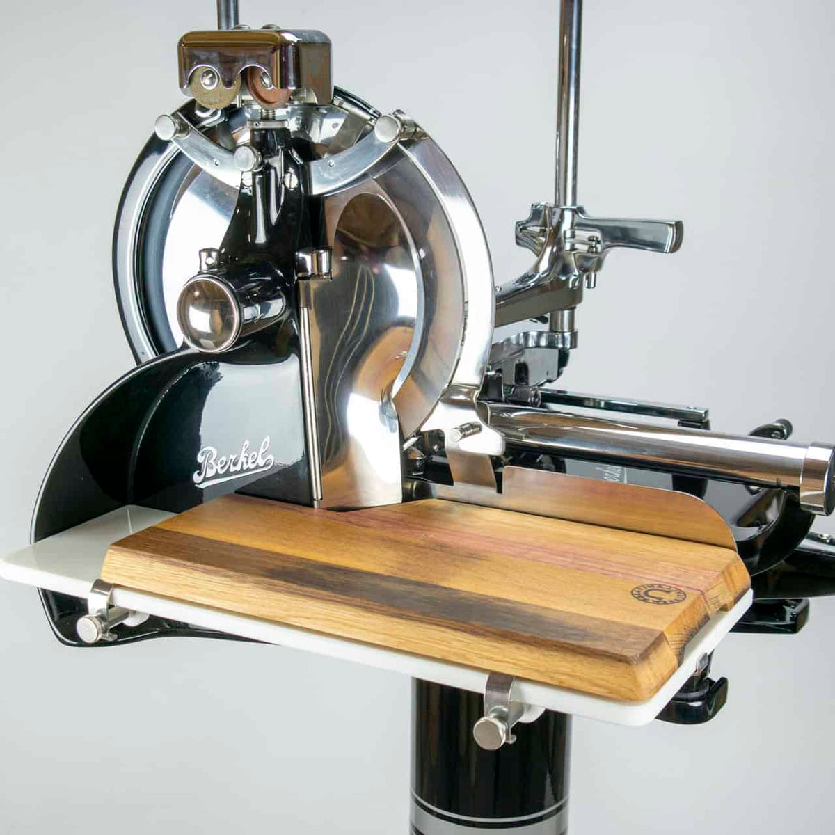 Eine Nahaufnahme der Berkel Volano P15 schwarz manuelle Aufschnittmaschine mit Schwungrad+ Aufschnittbrett, die ihre glänzenden Metallteile und das Holzschneidebrett zeigt. Dieser Fleischschneider verfügt über ein poliertes Retro-Design mit sichtbaren mechanischen Komponenten und einem eleganten Schwungrad.