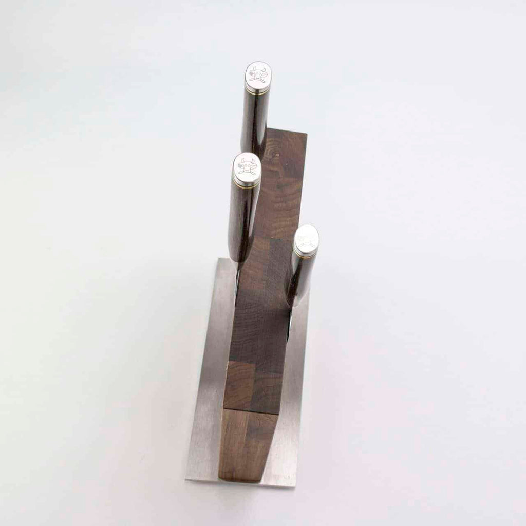 Eine Draufsicht auf drei Damastmesser mit dunklen Griffen in einem Exklusiven Messerblock-Set, bestehend aus einem KAI Shun Tim Mälzer Damastmesser und einem hochwertigen Böker Magnetmesserblock mit Metallsockel, platziert auf einer weißen Oberfläche.