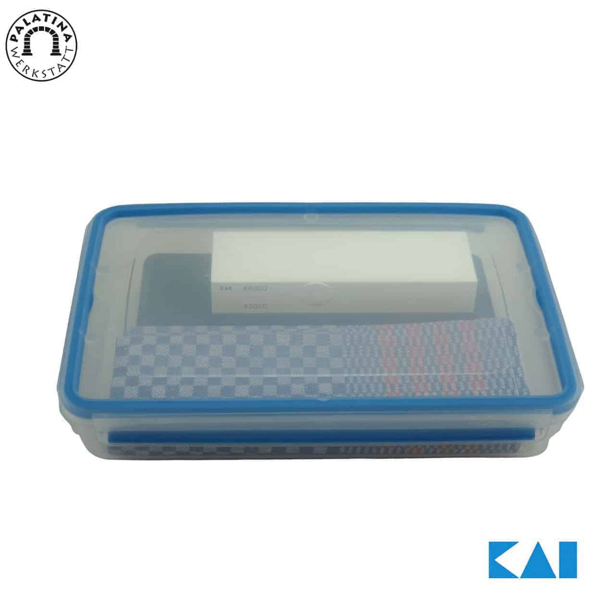 Eine rechteckige, transparente Plastikbox mit blauem Rand, die einen weißen Artikel und zwei karierte Tücher enthält. Die Box zeigt das Kai-Logo in der unteren rechten Ecke und ein rundes Logo mit dem Text „Kalatma Yeksta“ in der oberen linken Ecke. Es scheint Teil des hochwertigen 4-teiligen Schleifstein- und Pflegesets AP-0316 von Kai zu sein.