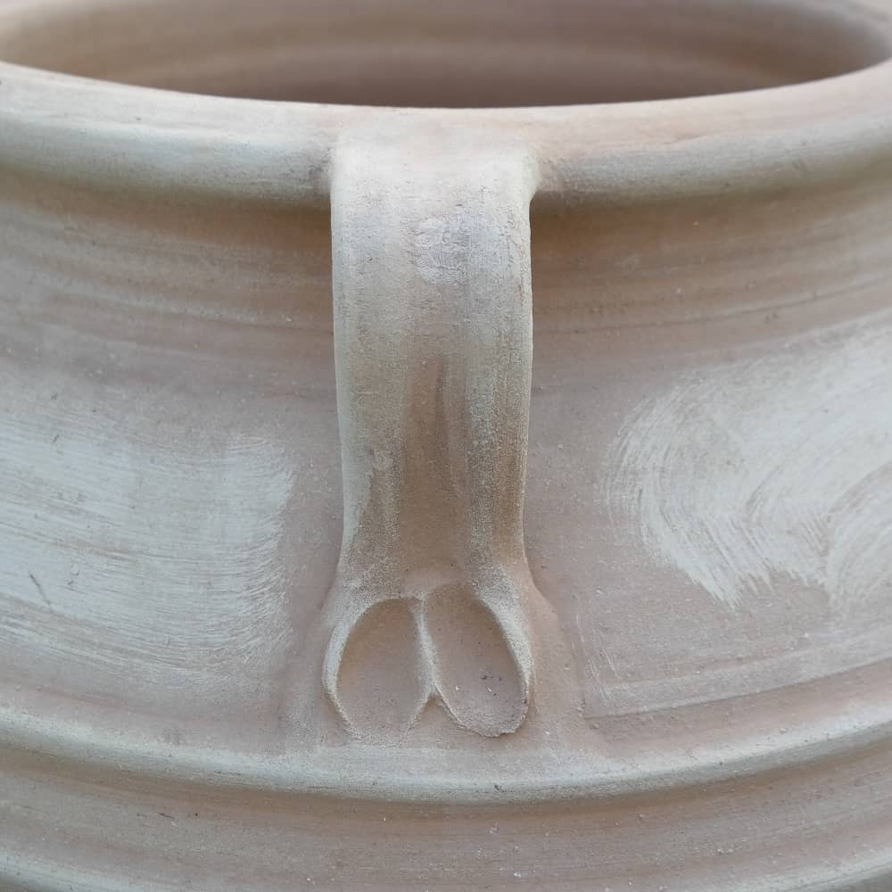 Eine Nahaufnahme der großen frostfesten Terrakotta-Amphore „Datura“ H= 90 cm, die einen Griff mit einem Paar geformter Füße an der Basis zeigt. Die Oberfläche der Amphore ist glatt, mit einigen sichtbaren Strukturdetails im Bereich des Griffs, die an das klassische Datura-Design erinnern.