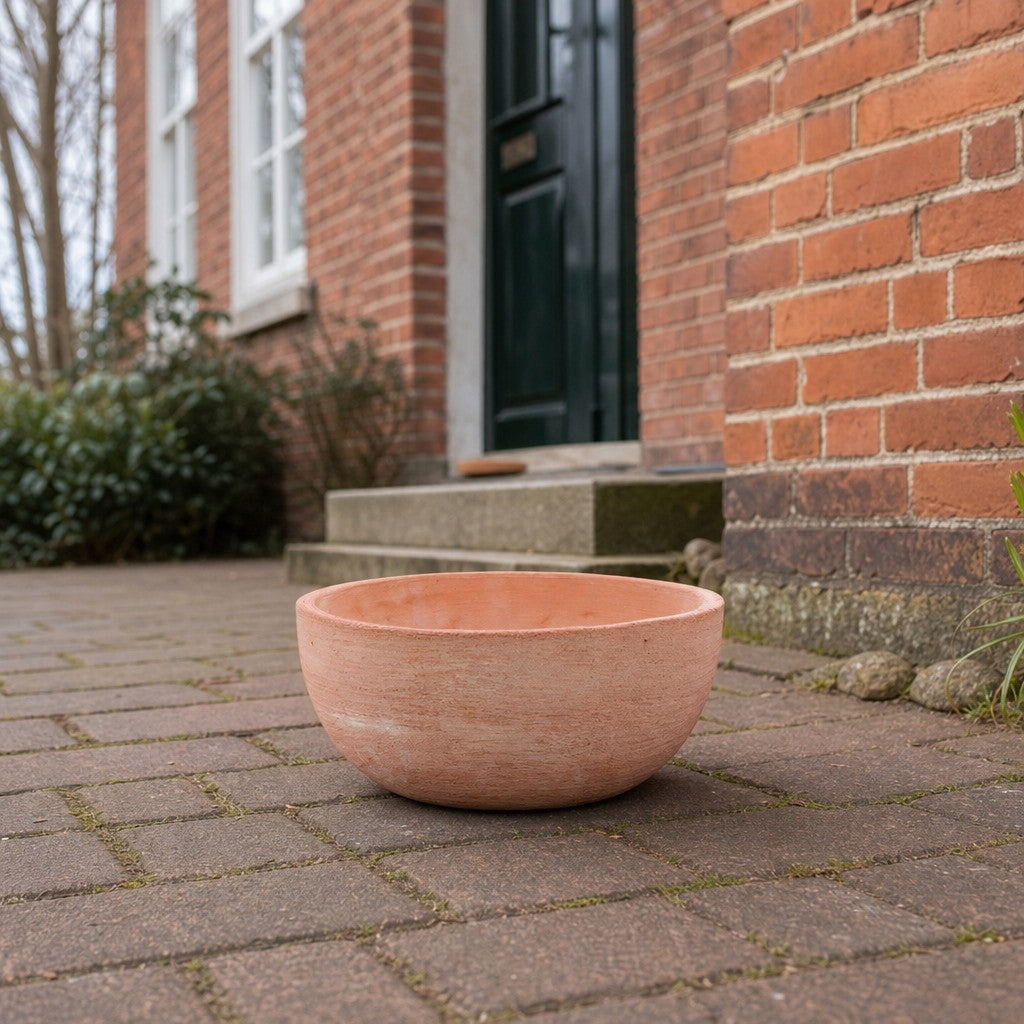 Eine moderne Pflanzschale mit einem Durchmesser von 29–50 cm steht leer auf einem Ziegelweg vor einem Haus mit roten Backsteinwänden, einer grünen Tür und Sträuchern in der Nähe des Eingangs.