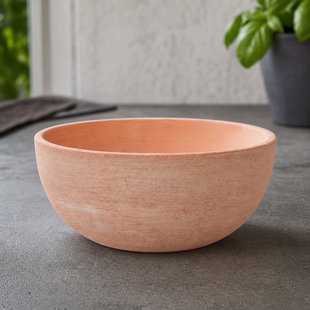 Eine moderne Pflanzschale aus Terrakotta mit einem Durchmesser von 29–50 cm steht leer auf einer grauen Arbeitsfläche; im unscharfen Hintergrund ist eine grüne Topfpflanze zu sehen.