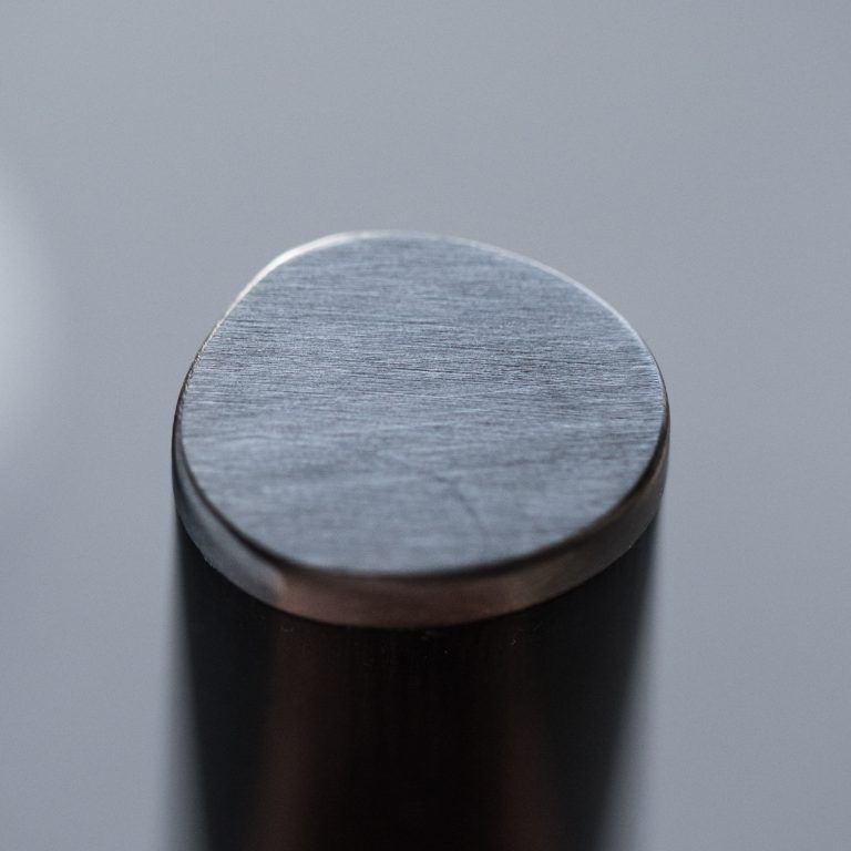 Nahaufnahme der Oberseite eines zylindrischen Metallstabs mit glatter, leicht ovaler Oberfläche und gebürstetem Finish. Der Hintergrund ist unscharf, wodurch die Textur und die Details der Metalloberfläche hervorgehoben werden, was an die Handwerkskunst des KAI Weihnachtsangebots 2-teiliges Geschenkset – Shun Classic – limitiertes 1.200-Stück-Set erinnert.