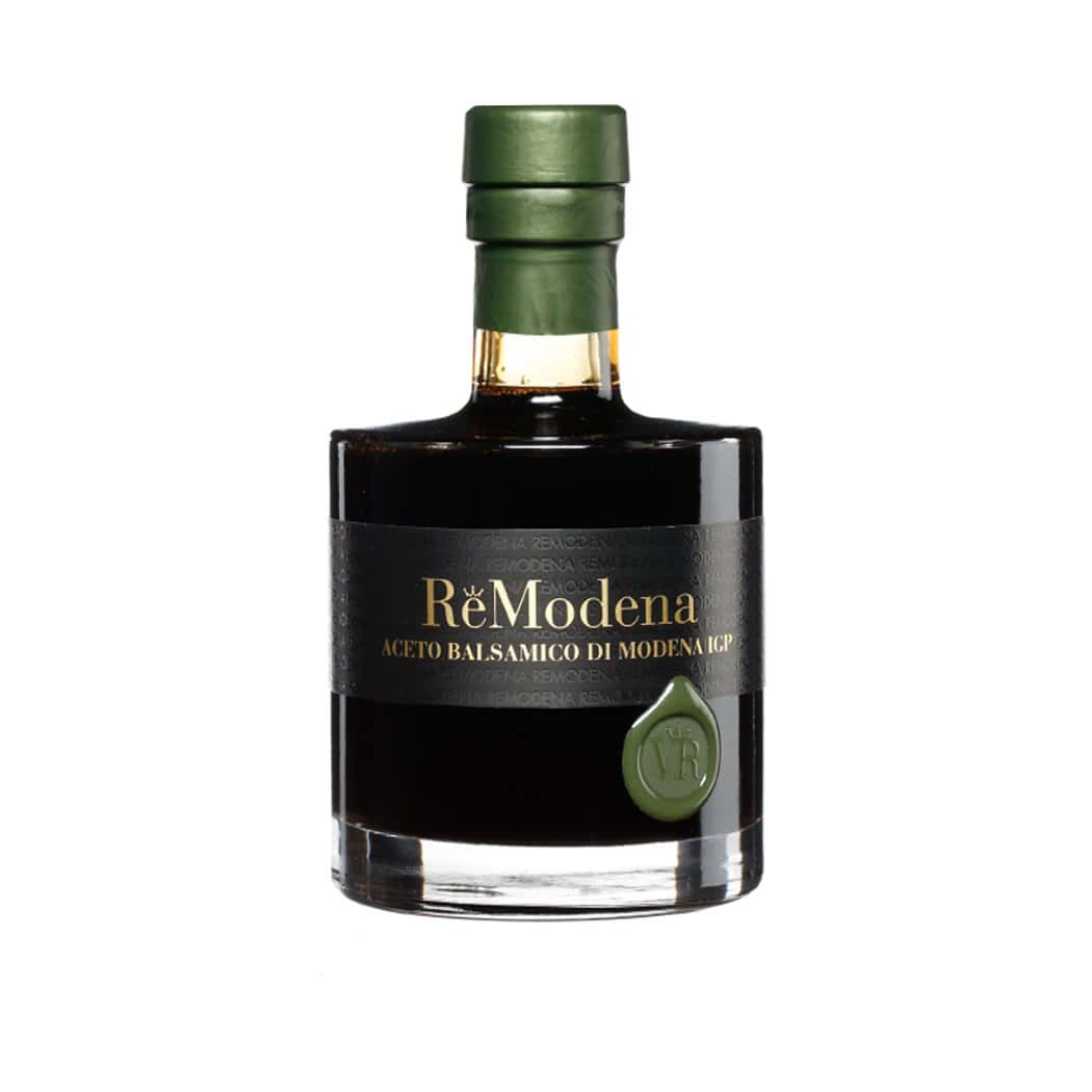 Eine Glasflasche mit grünem Verschluss enthält dunklen Balsamico-Essig mit der Aufschrift „ReModena Balsamico Essig 250 ml verschiedene Sorten“ auf schwarzem Etikett. Die Flasche, geschmückt mit einem grünen Wachssiegel und Goldfolienakzenten am Flaschenhals, präsentiert den exquisiten Balsamico aus Modena. Der Hintergrund ist schlicht weiß.
